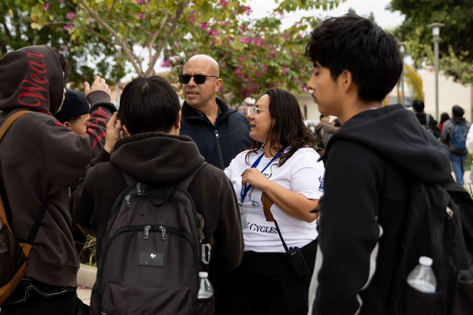 Adults and teens stand in a group outside talking.