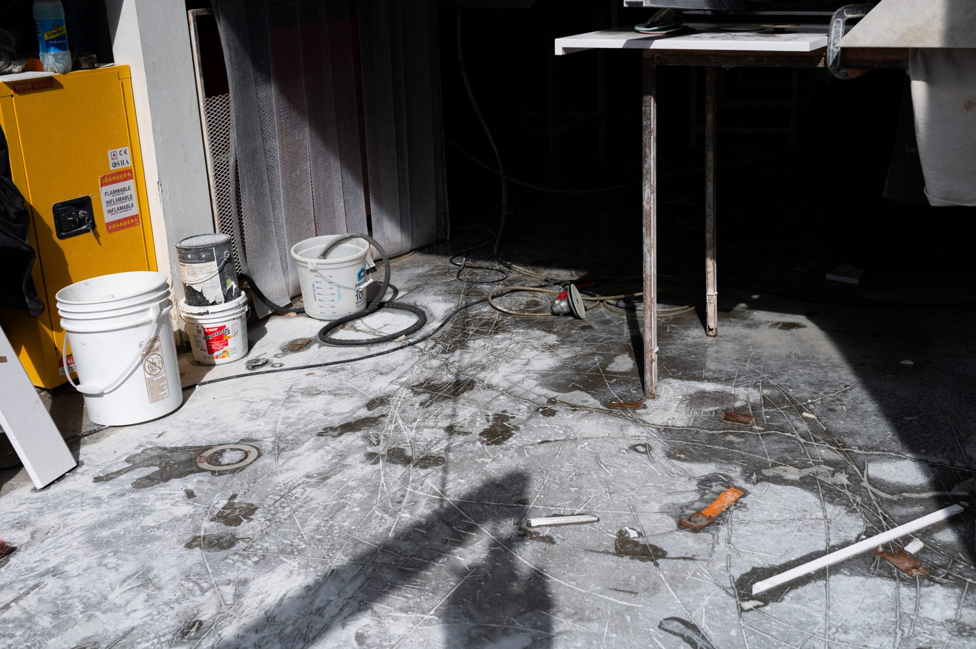 A workshop floor covered in dust with buckets in the corner