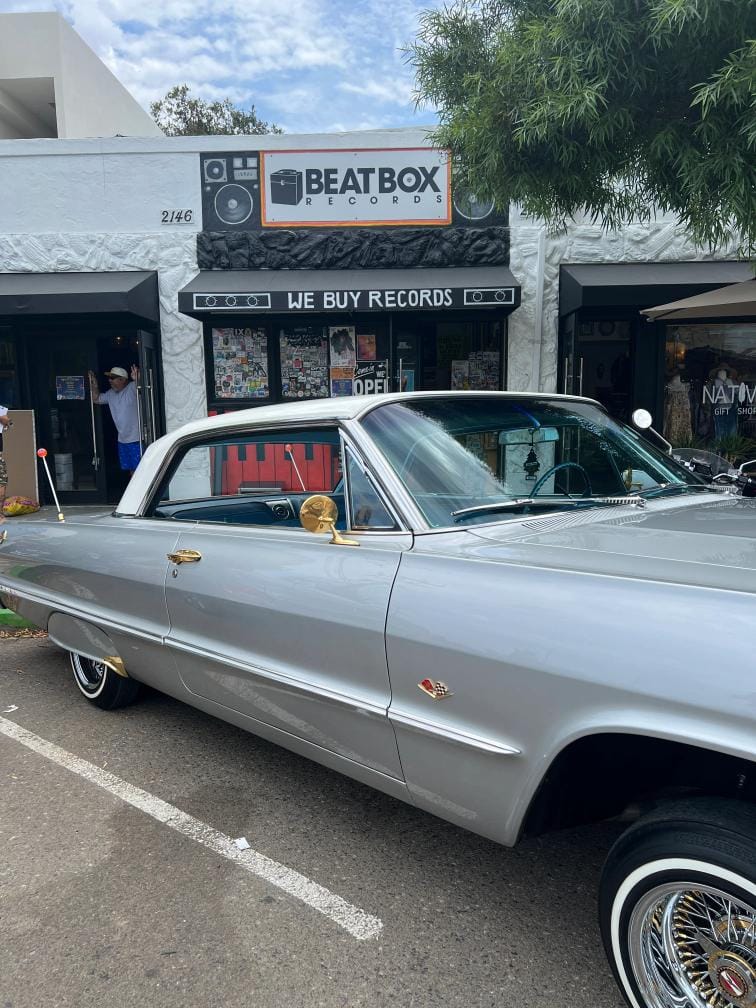 A lowrider car is parked in front of a storefront with a sign that says Beatbox Records