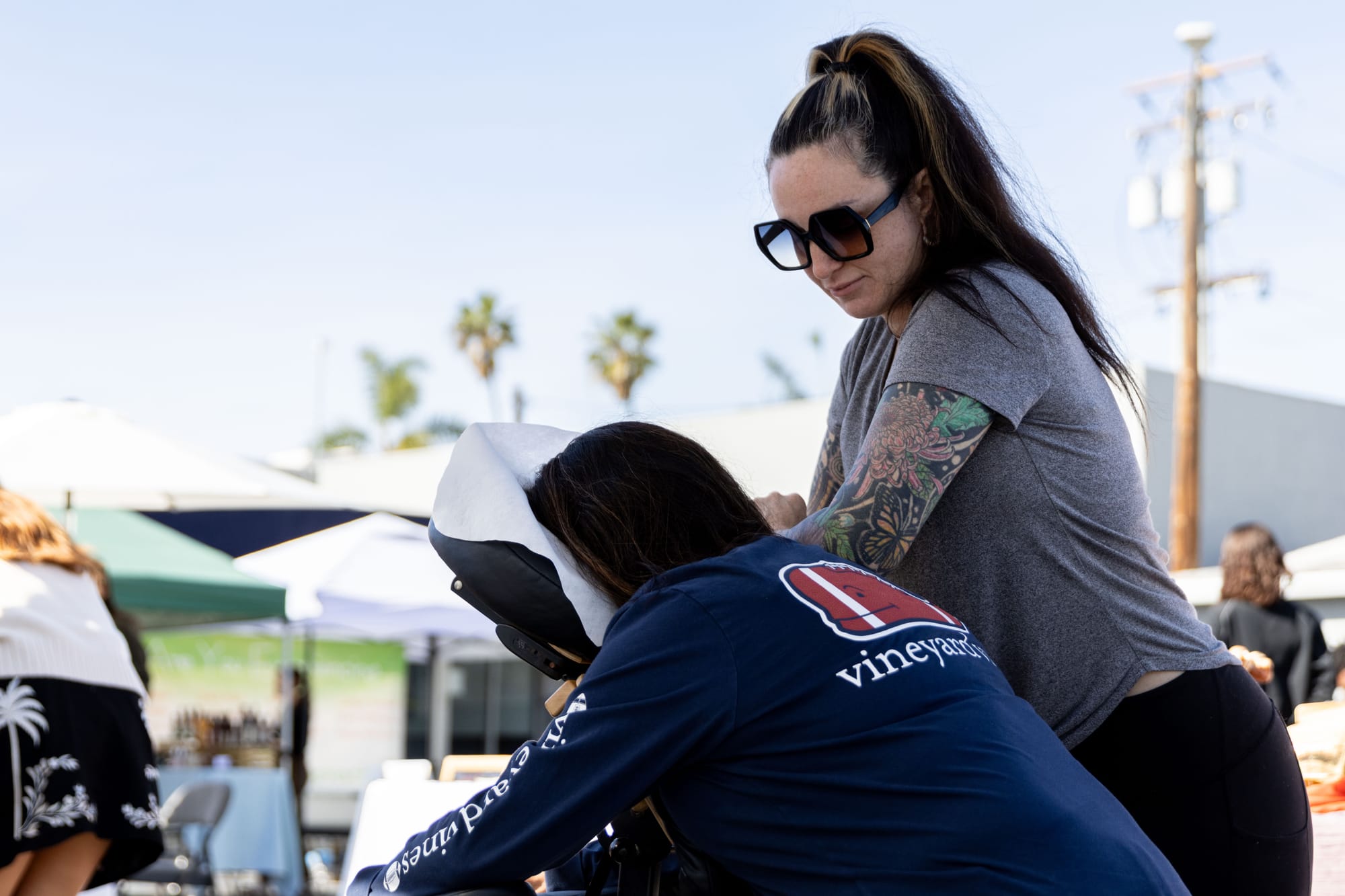 A woman gives a chair massage to someone during an open air market