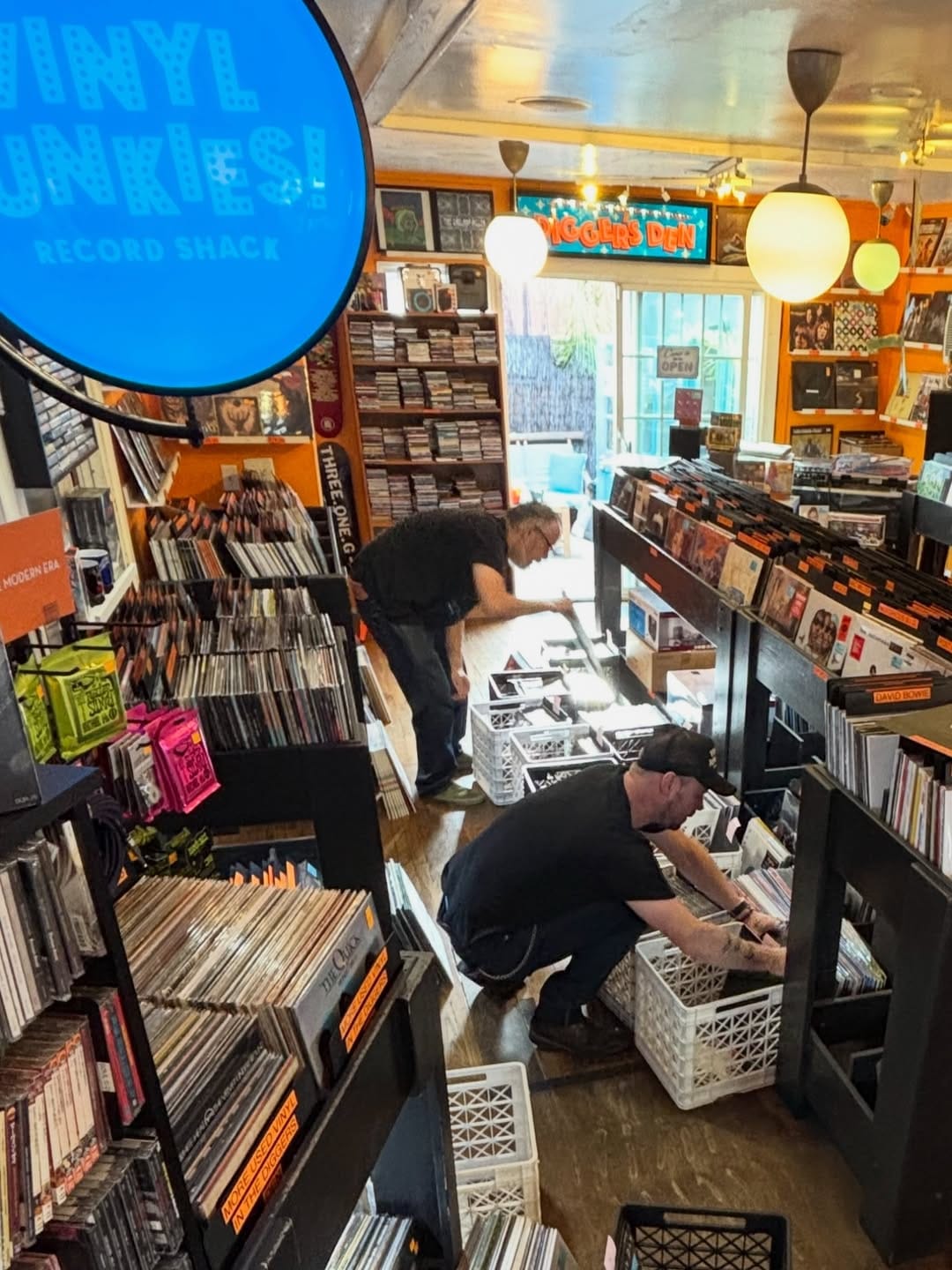 Two men wearing all black bend over crates of records in the middle of a record store