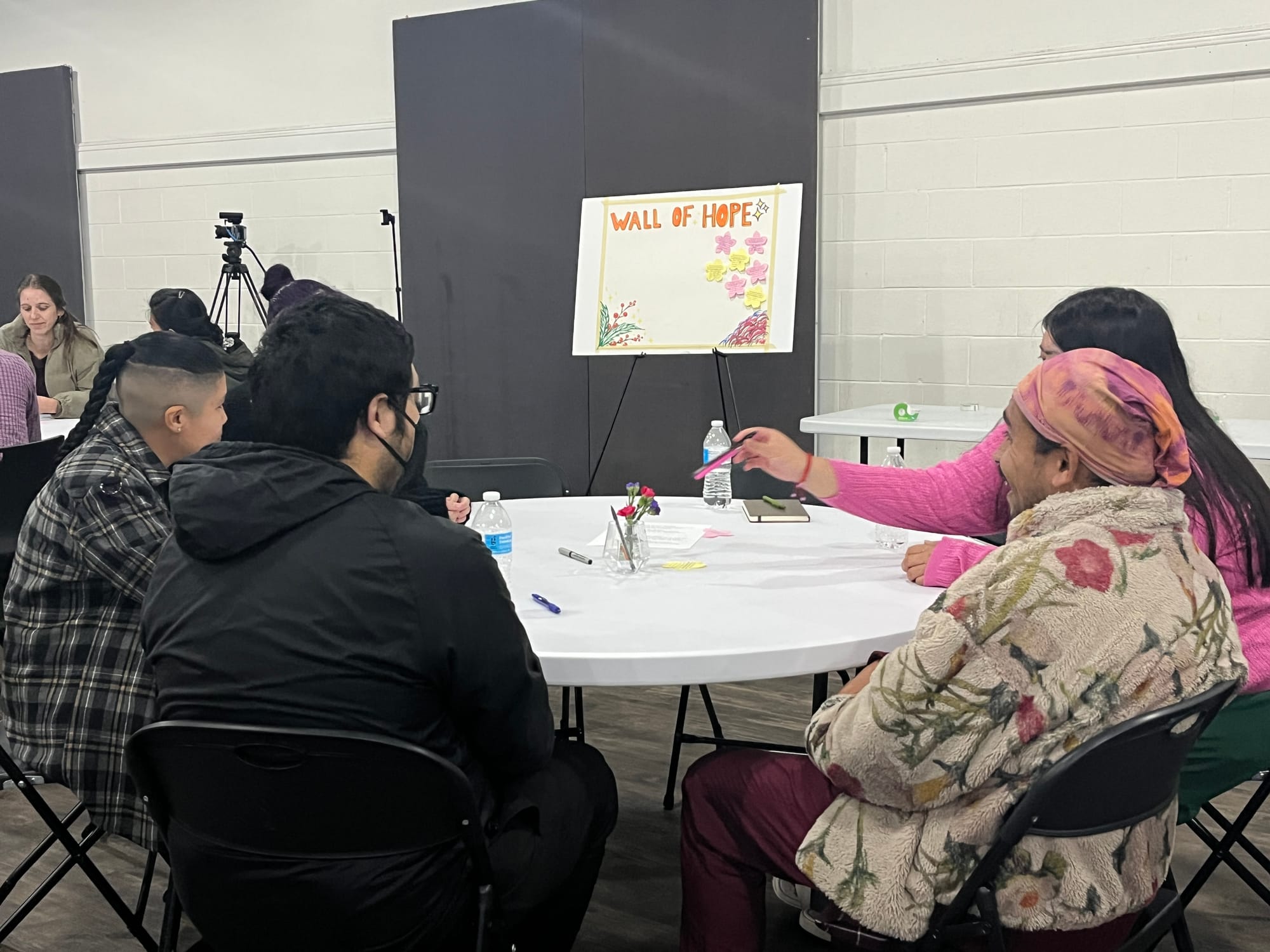 Four people sit and discuss at a round table while one of them grabs a pen in the middle of the table