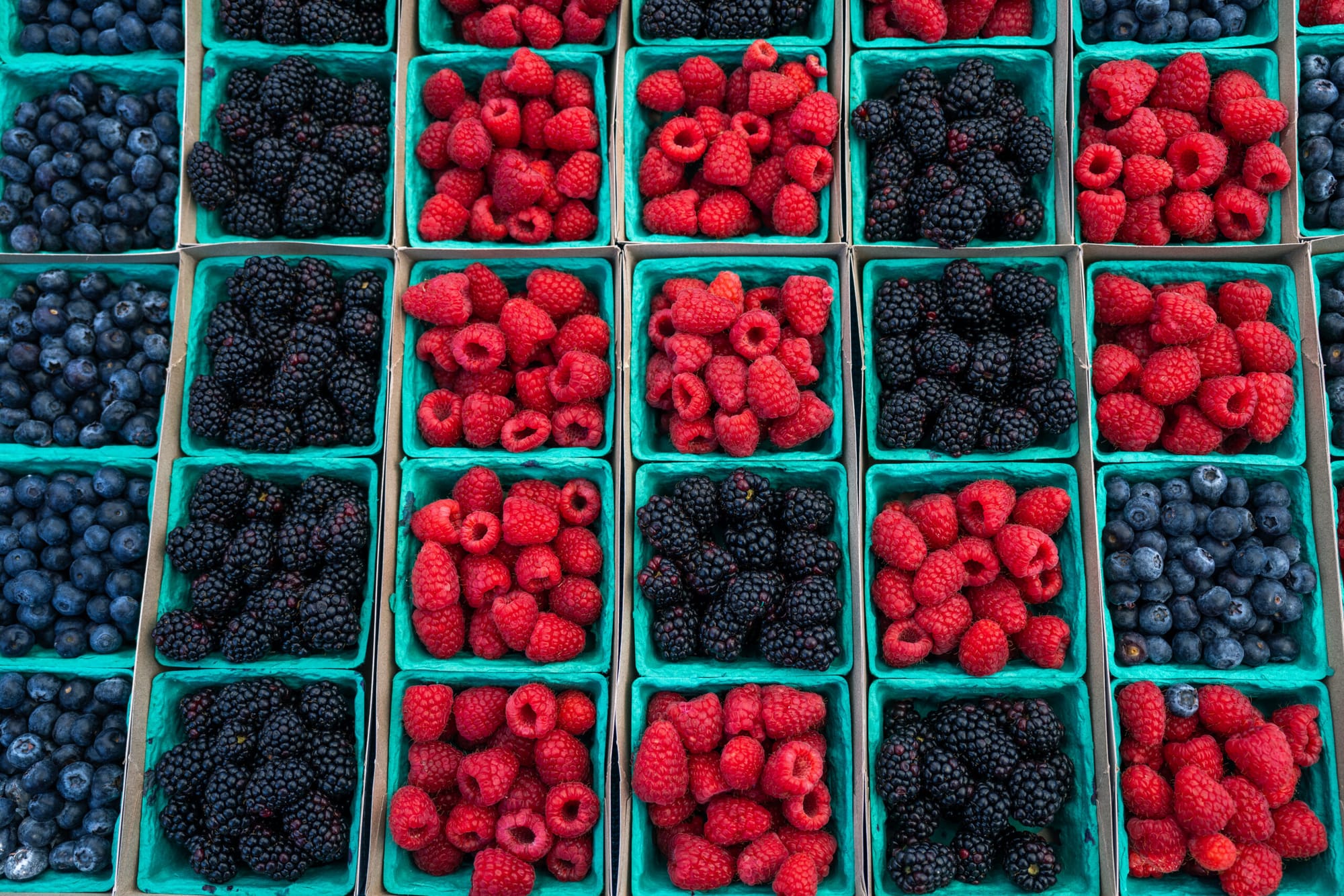 Blueberries, blackberries and raspberries in green containers on a table