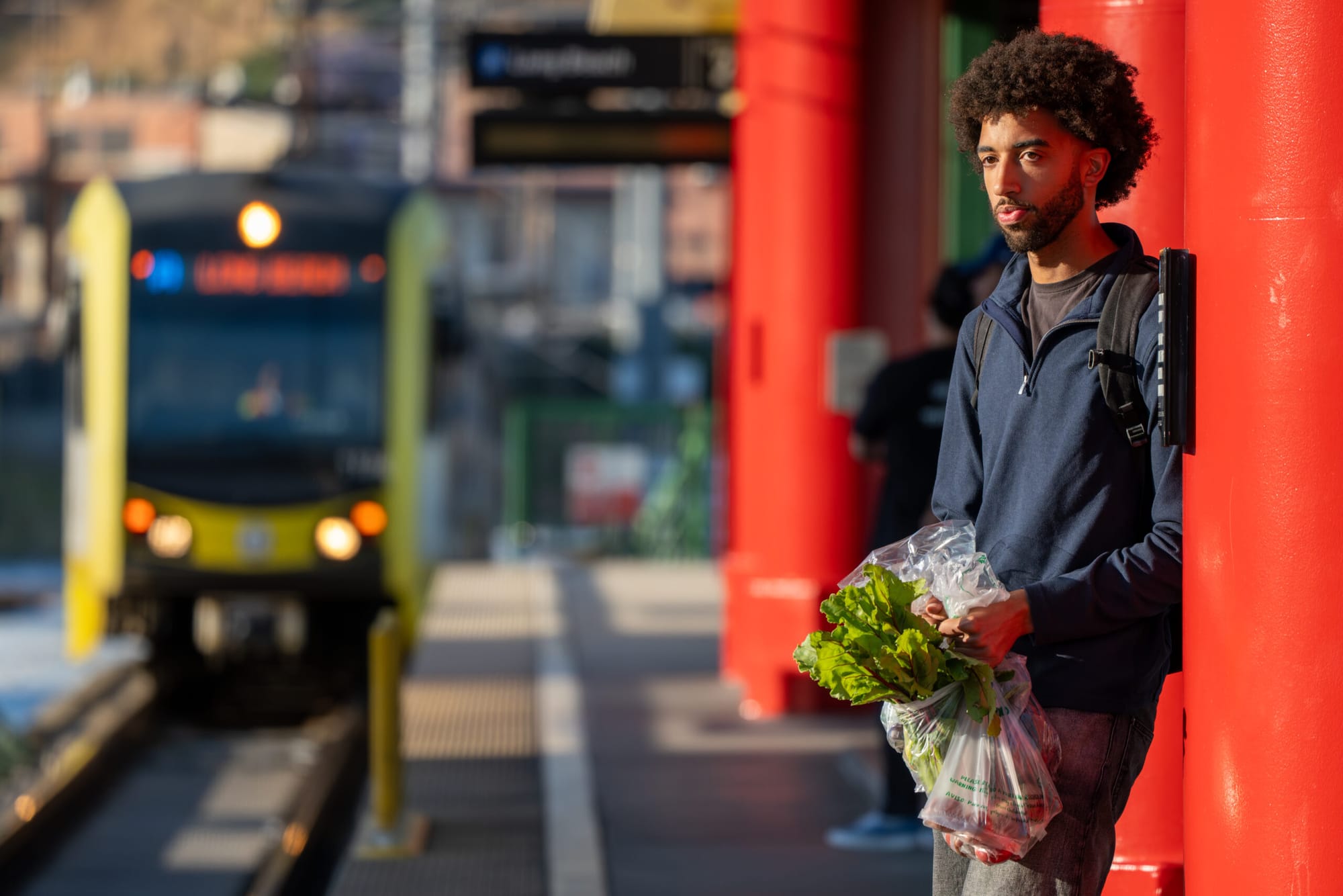 A person holds a bag of vegetable while standing at a trolley stop
