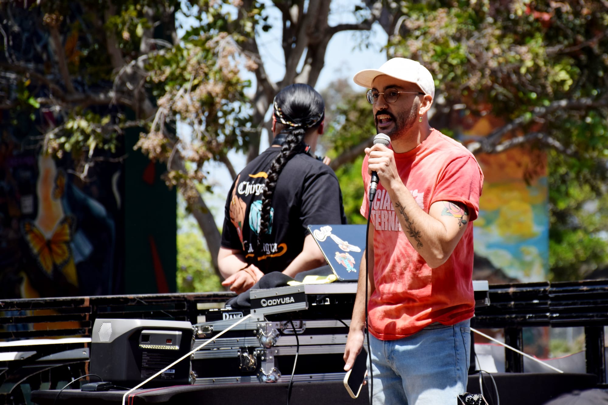 Someone in a red t-shirt speaks on a stage outside
