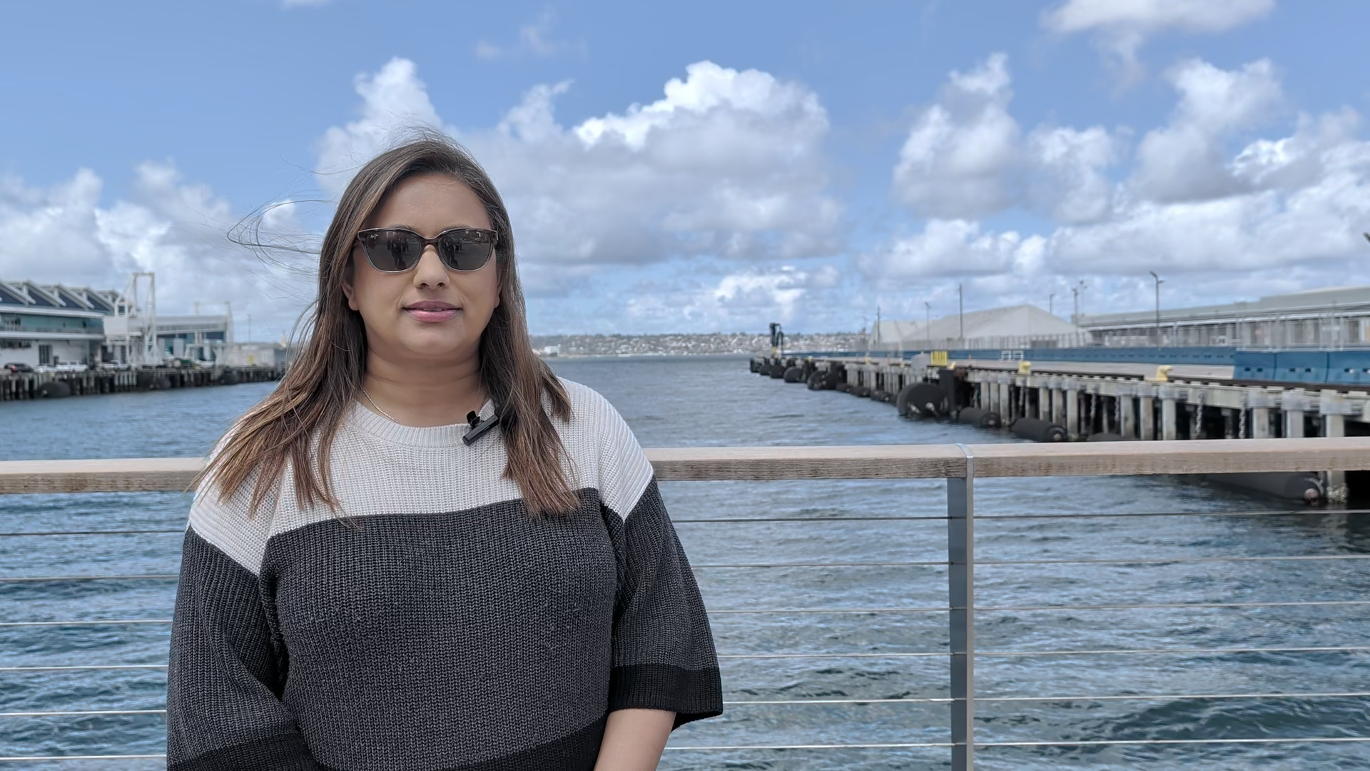 A woman in a gray and white sweater stands in front of a dock
