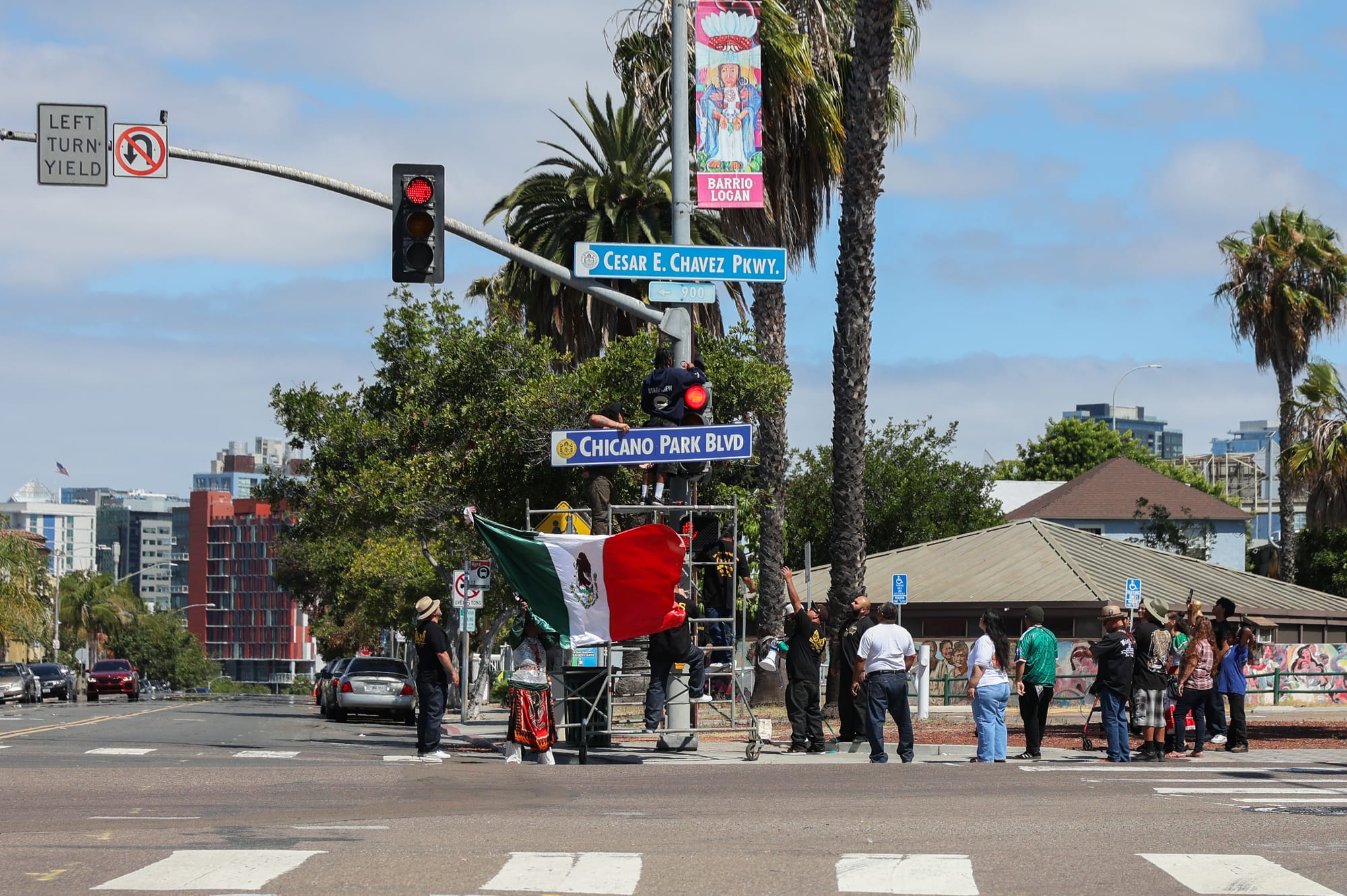 Someone holds a Mexican flag in front of scaffolding and a street light with a small crowd around them