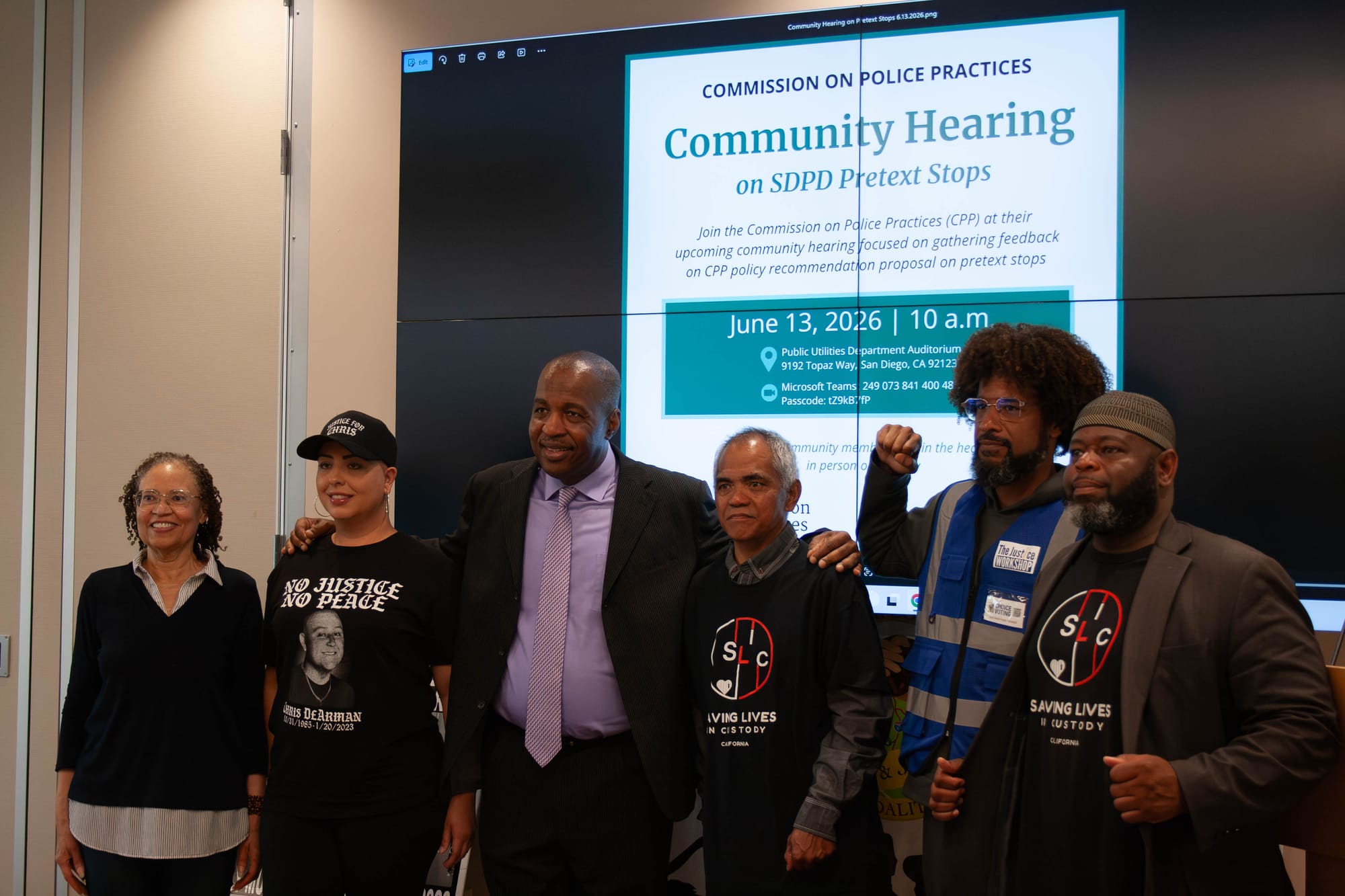 Six people wearing mostly black stand in front of a screen that says community hearing on SDPD pretext stops