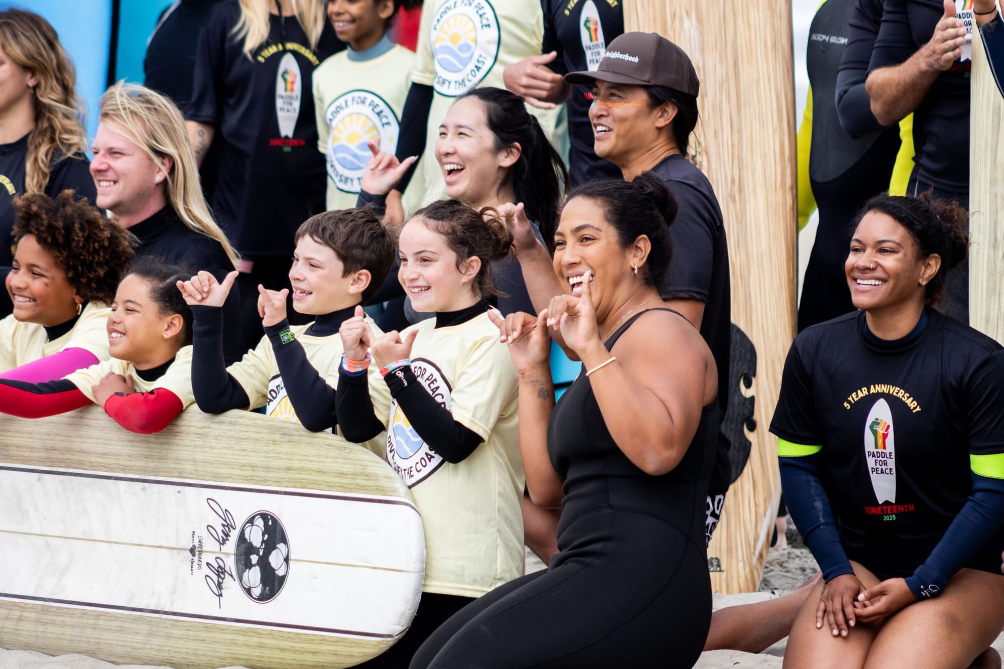 A group of people pose for a photograph in front of surfboards on the beach