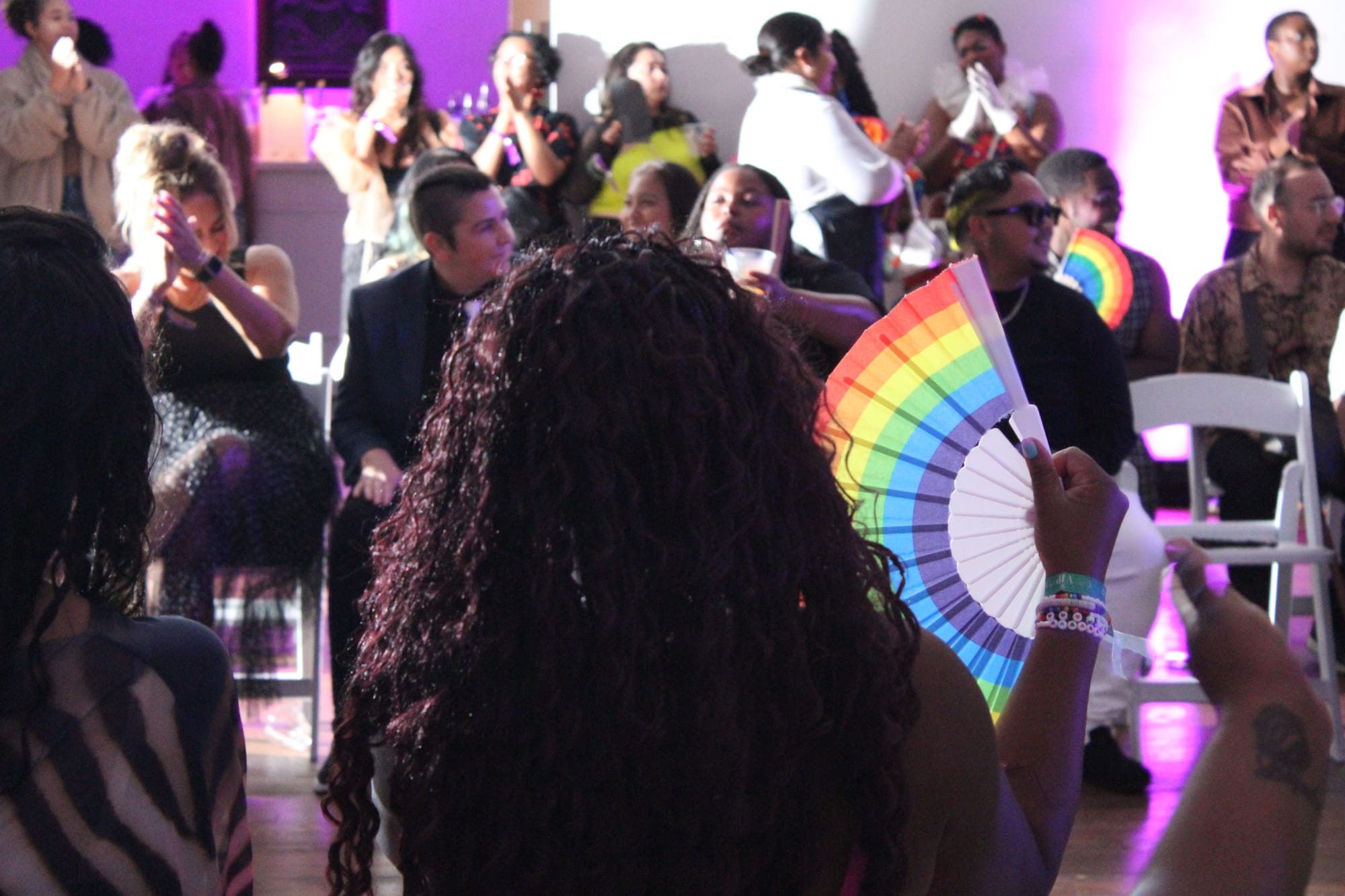 A person with long curly hair holds a rainbow fan