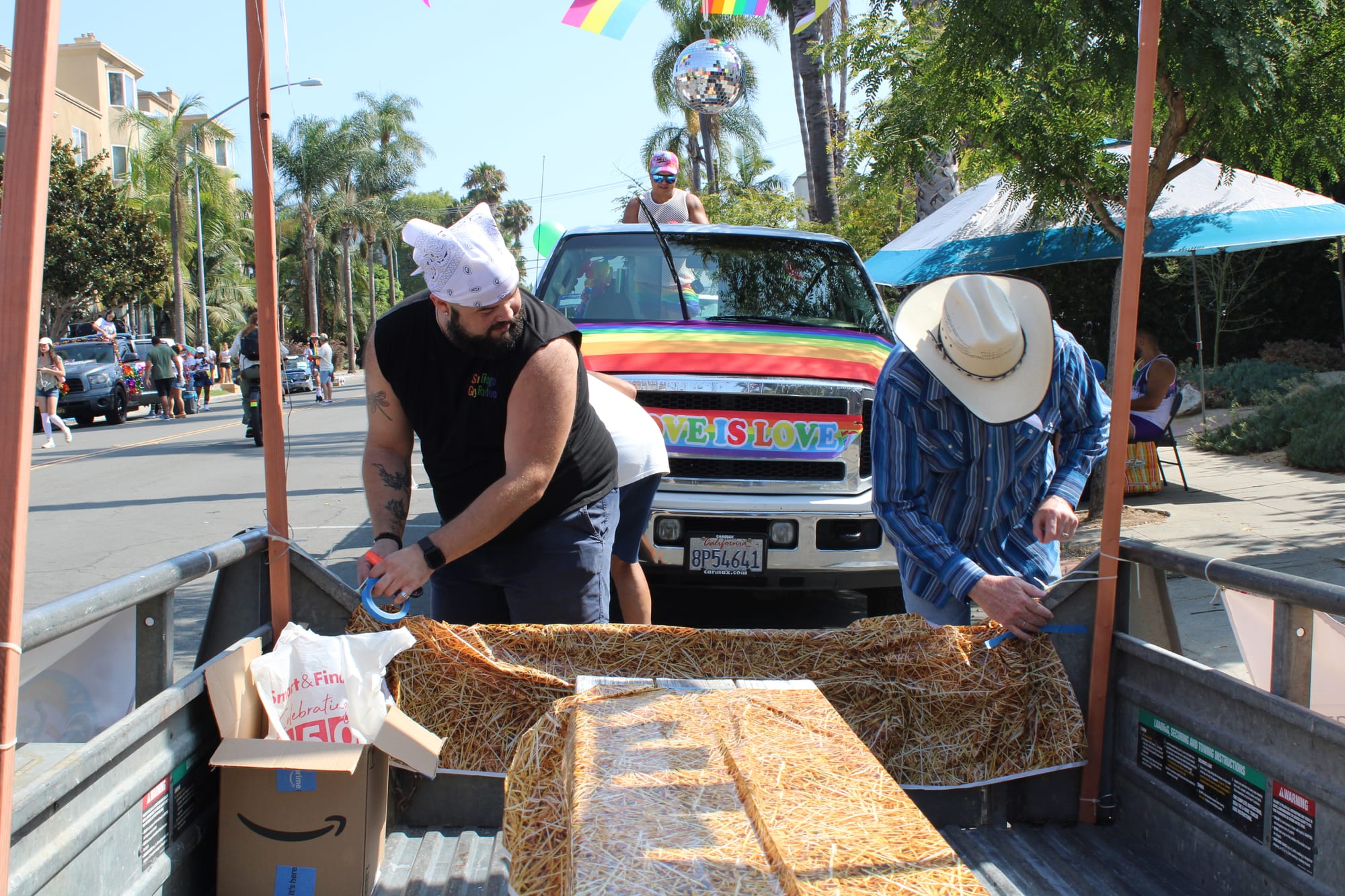 Two people tie hay bale printed tarps to a trailer