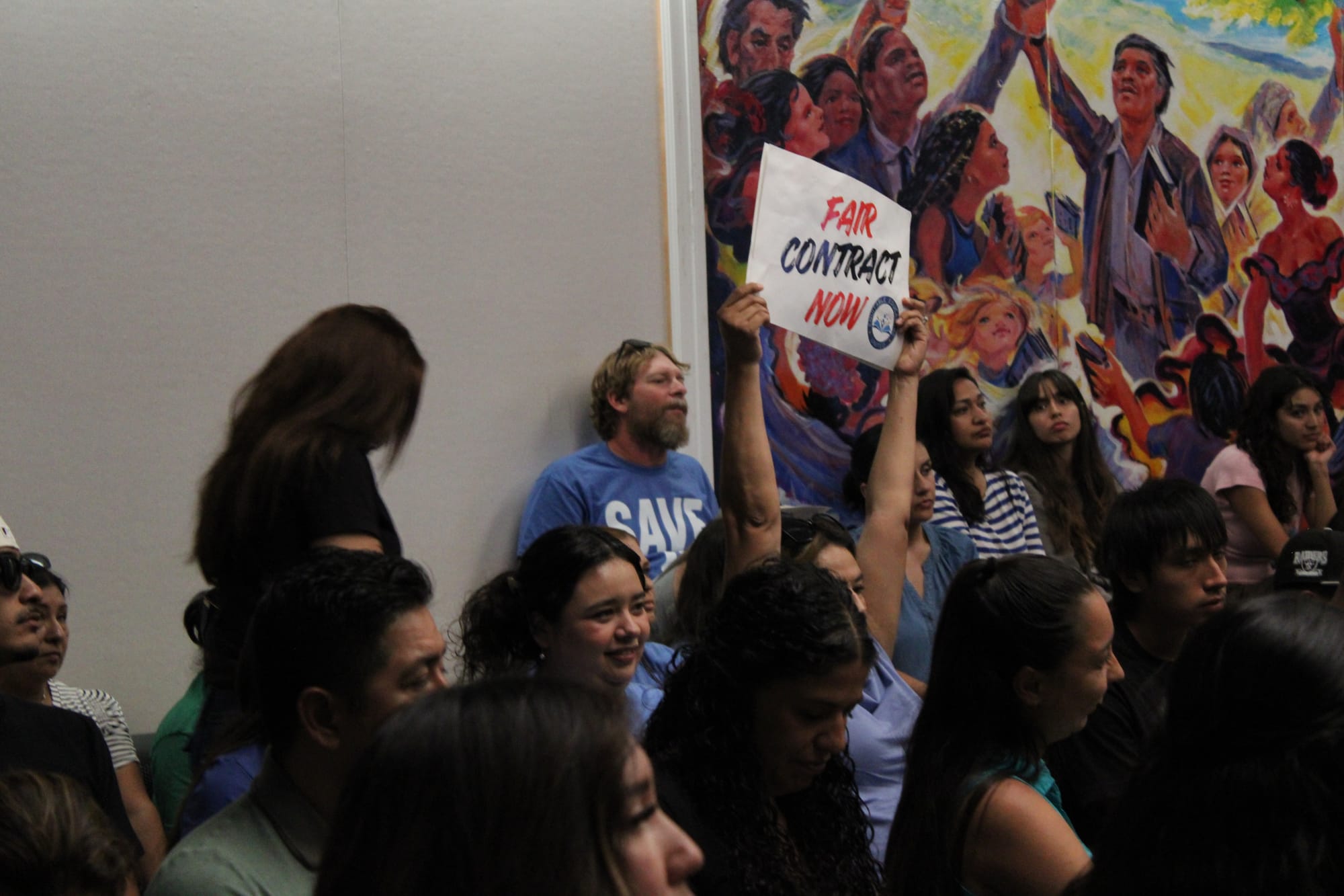 An audience member holds up high a “fair contract now” sign