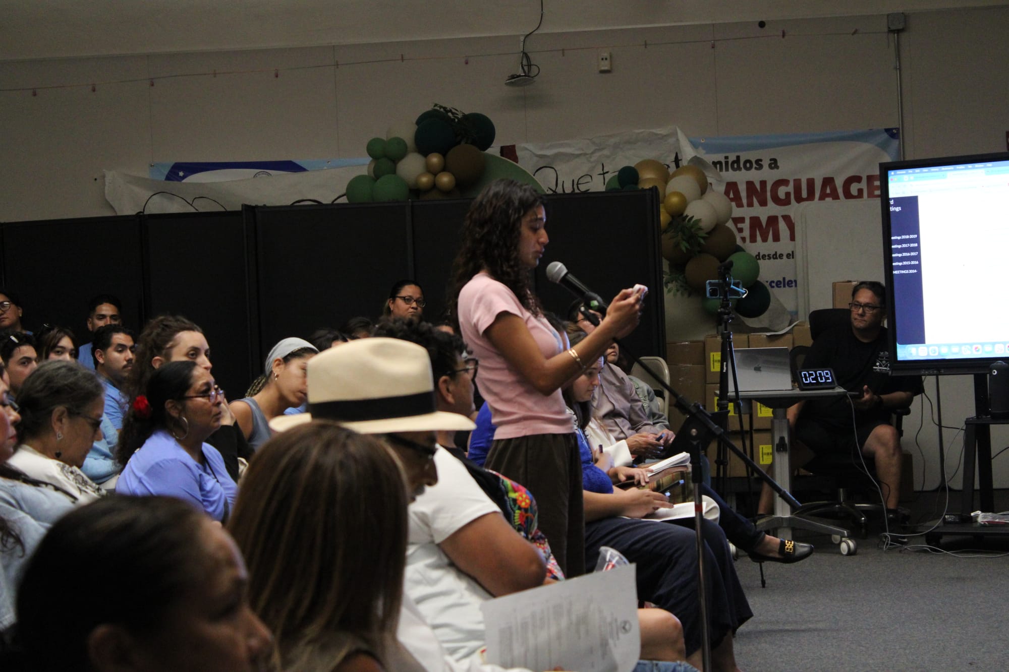 A girl in a pink shirt speaks into a microphone while crying 