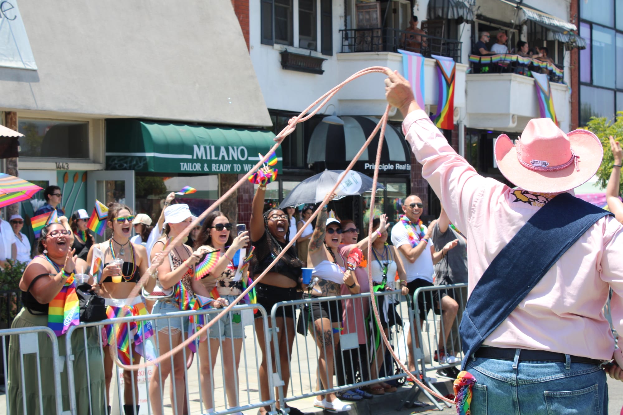 A person in a pink button down and pink cowgirl hat twirls a pink lasso in front of a parade crowd