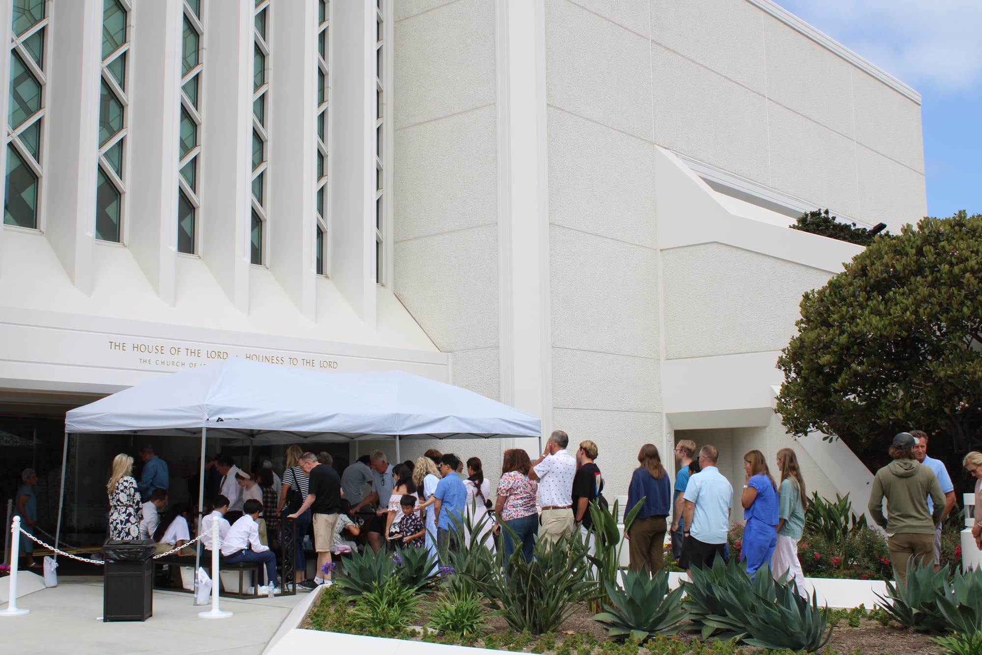 A line of people waiting at the entrance of a white temple 