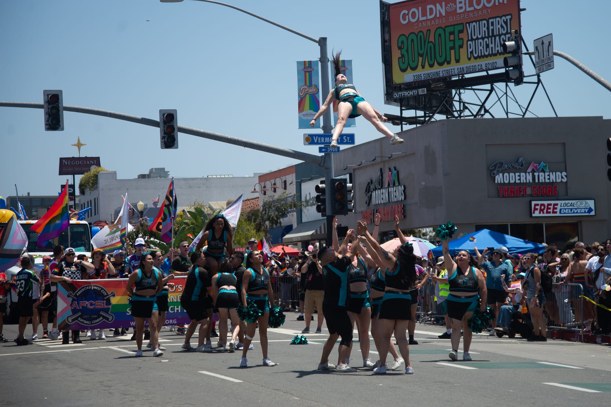 A group of cheerleaders stand under a cheerleader who is flying in the air, stomach to the sky, legs and arms spread wide.