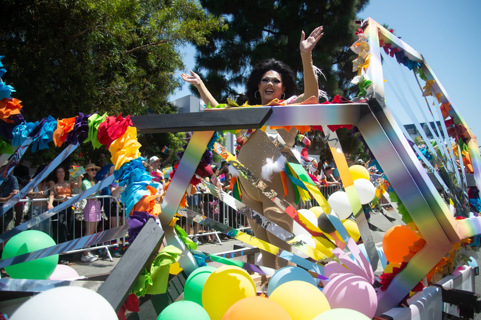 A person holds their arms up and smiles from inside a geometric structure on top of a float