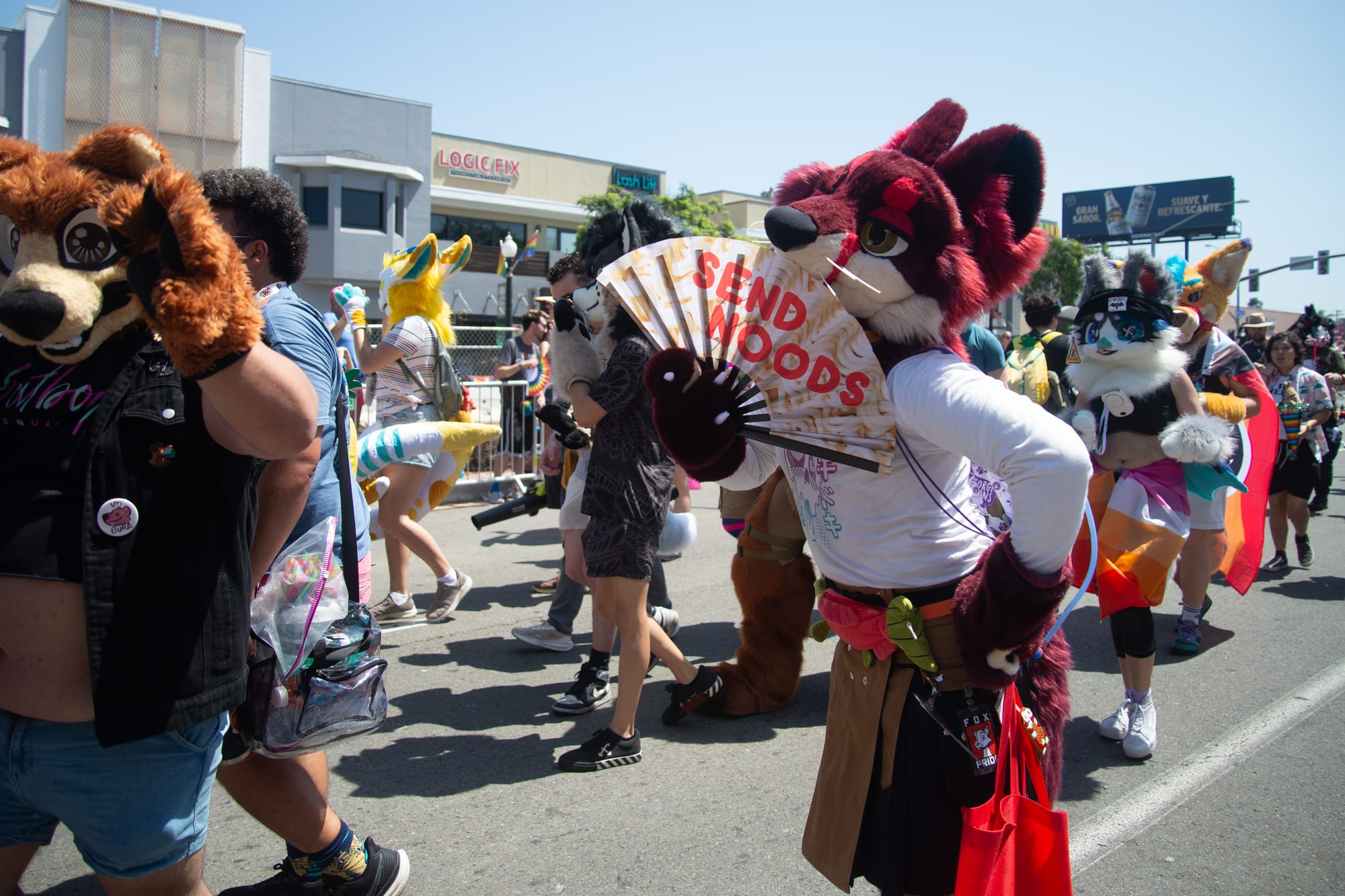 A person in a red fox costume holds up a fan that says "Send Noods."