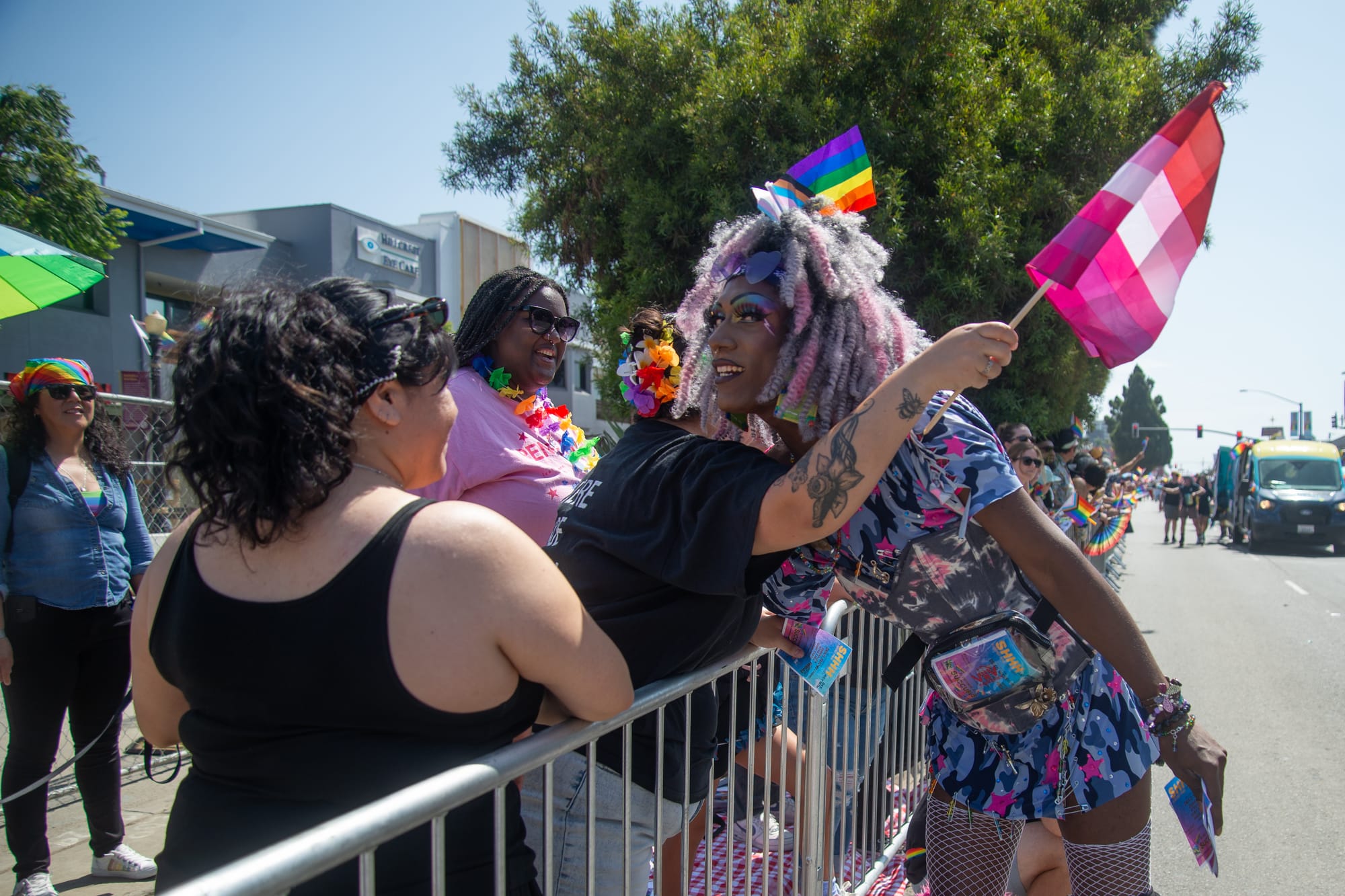 A person with a purple and pink dress and matching curly hair hugs a person in a black shirt