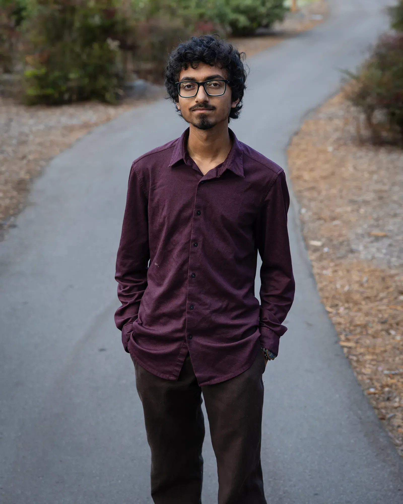 A person with a beard, glasses and a purple shirt looks straight into the camera