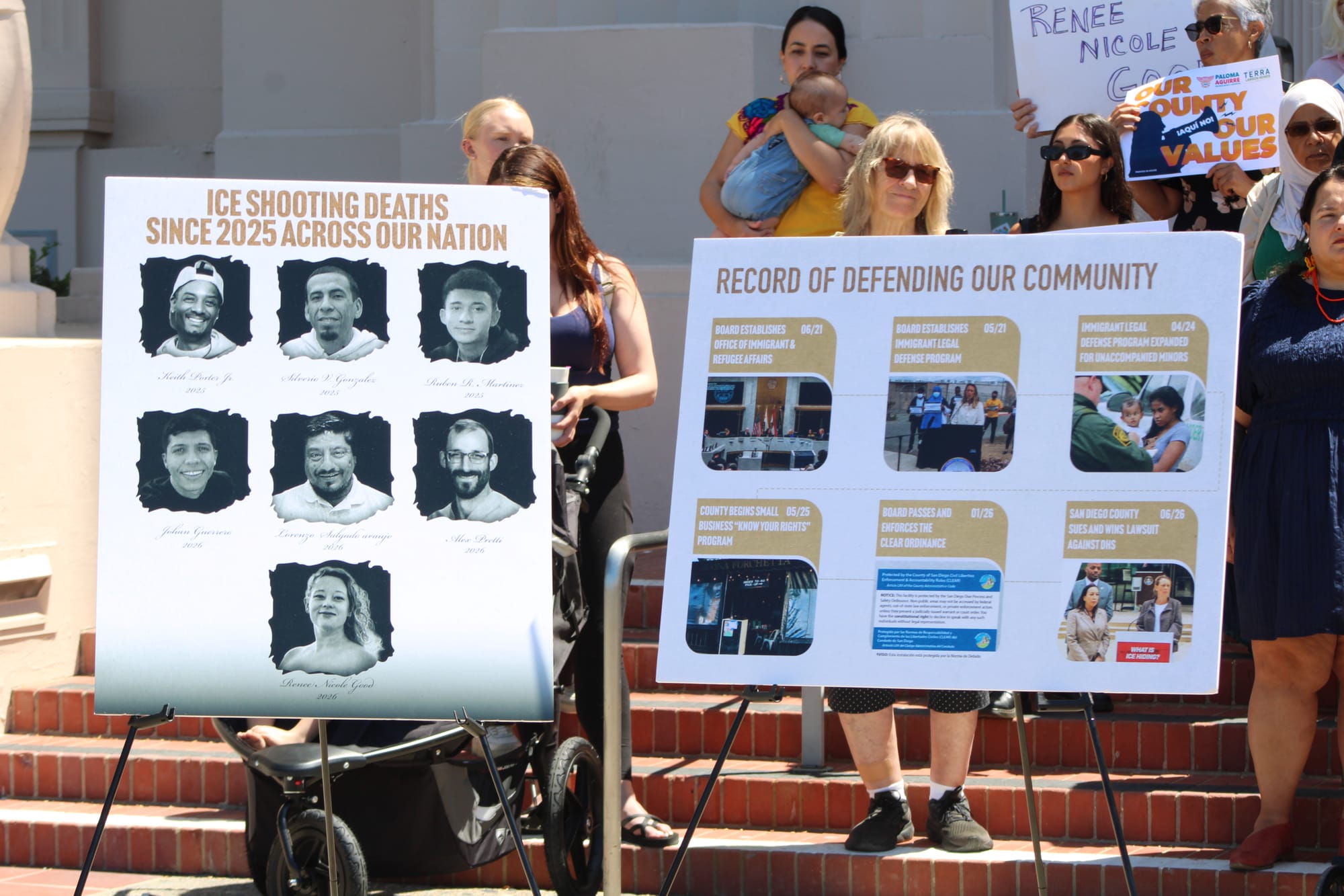 Two signs stand on easels in front of a crowd on brick steps