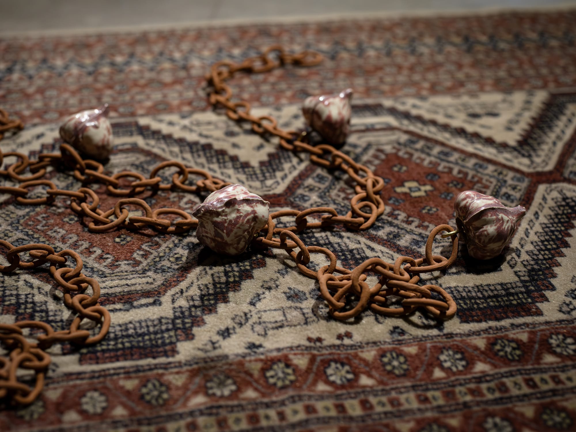 White and purple and rust colored ceramic garlic pieces lie on a rug connected by a rusted chain