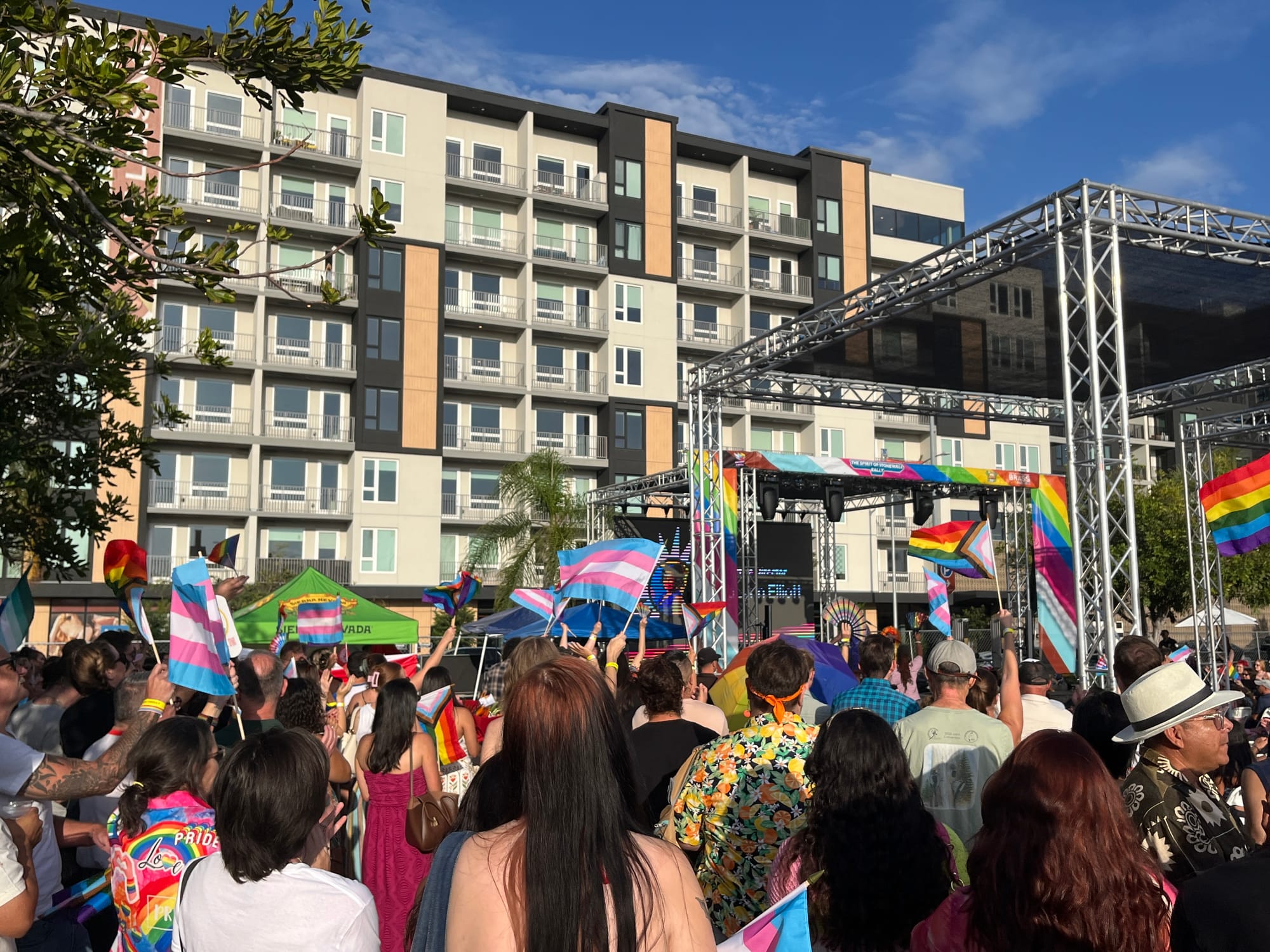 a crowd of people holding Pride flags face a large stage