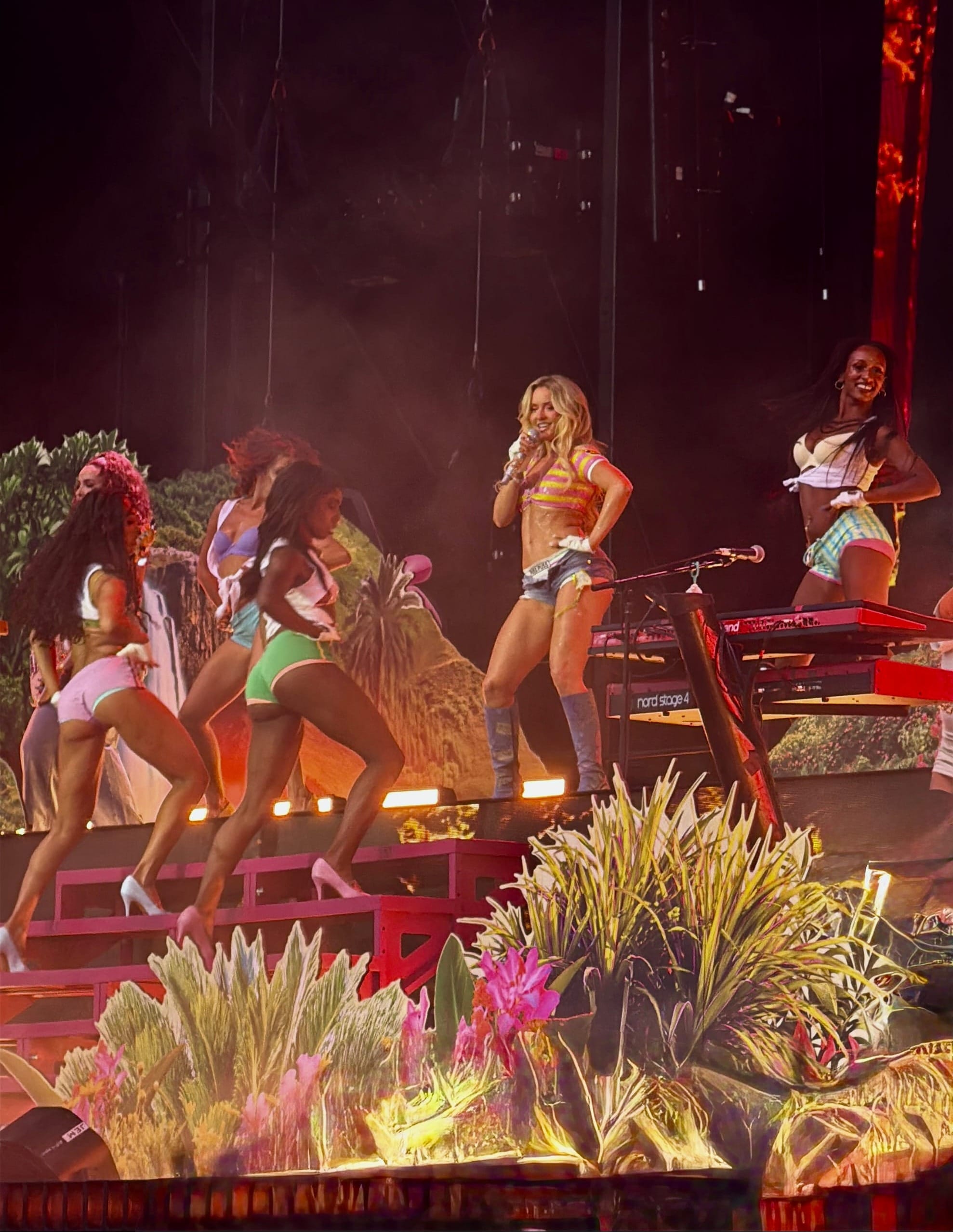 Zara Larsson performs on a brightly lit stage surrounded by dancers and tropical-themed set pieces at Lollapalooza.