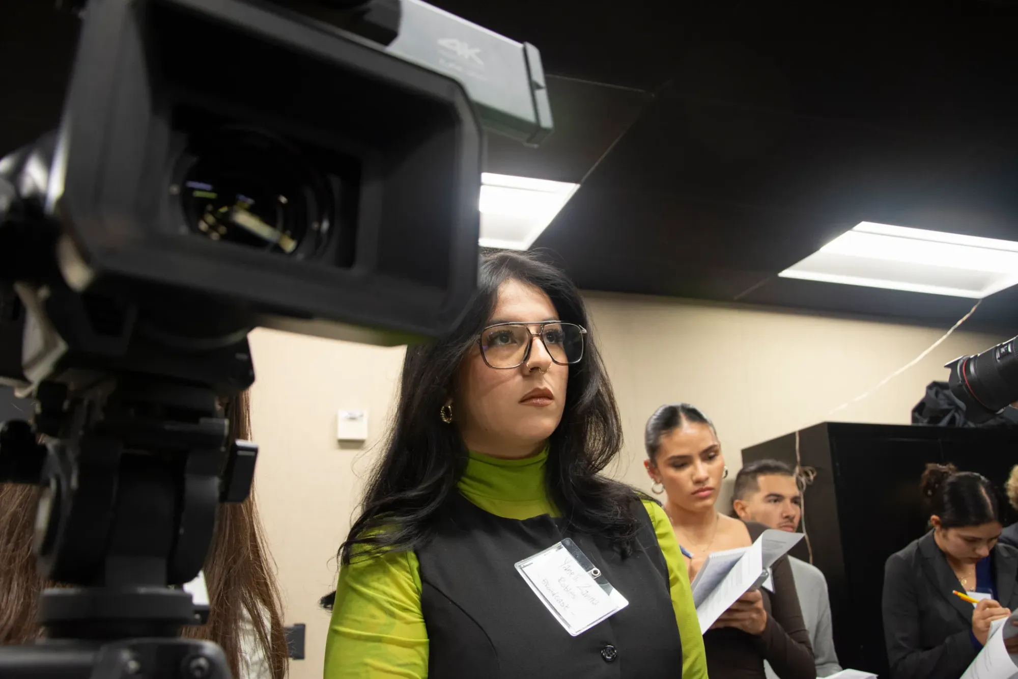 Picture of someone with glass and a bright green shirt next to a film camera