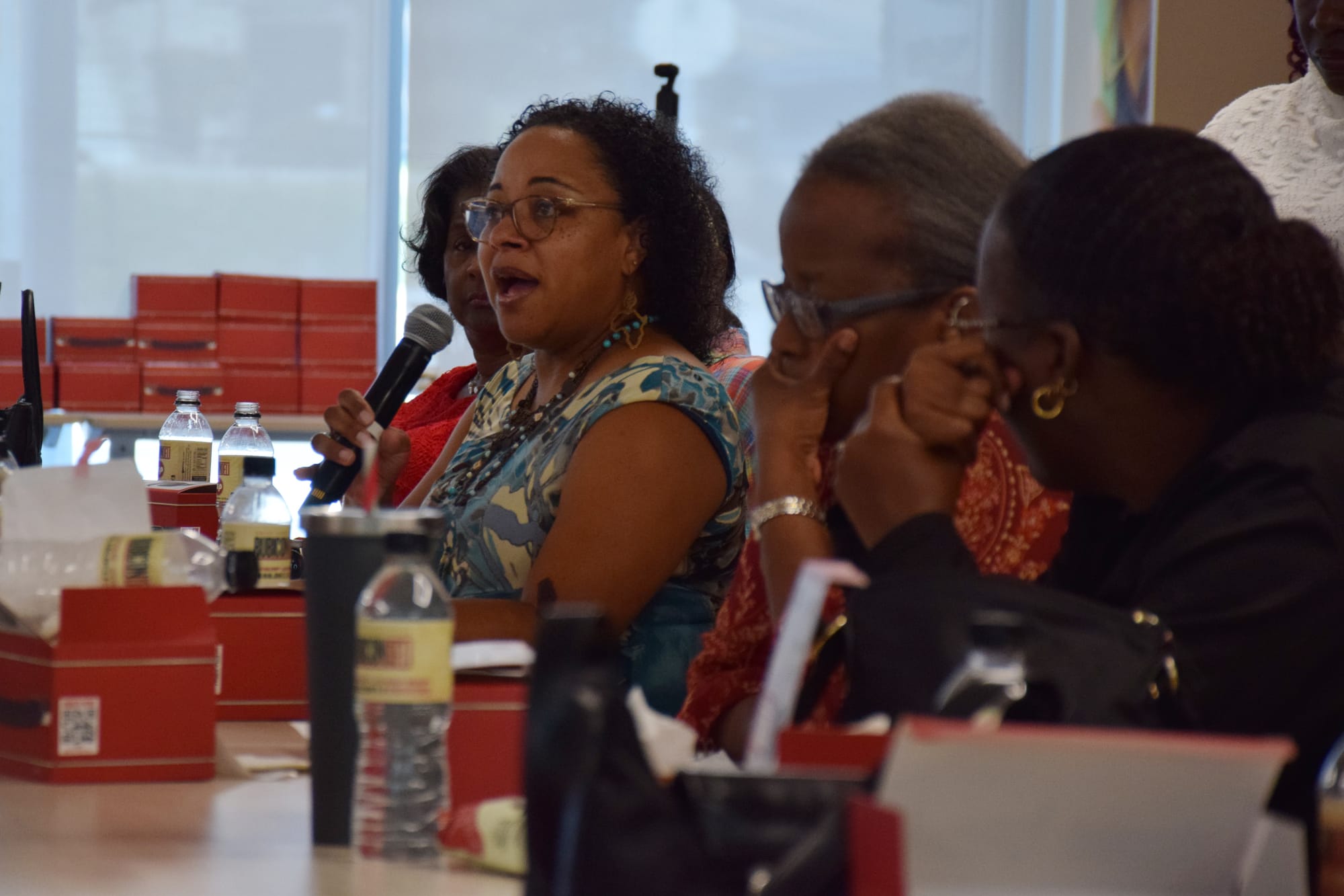 A person speaks into a microphone sitting next to other people at a luncheon. 