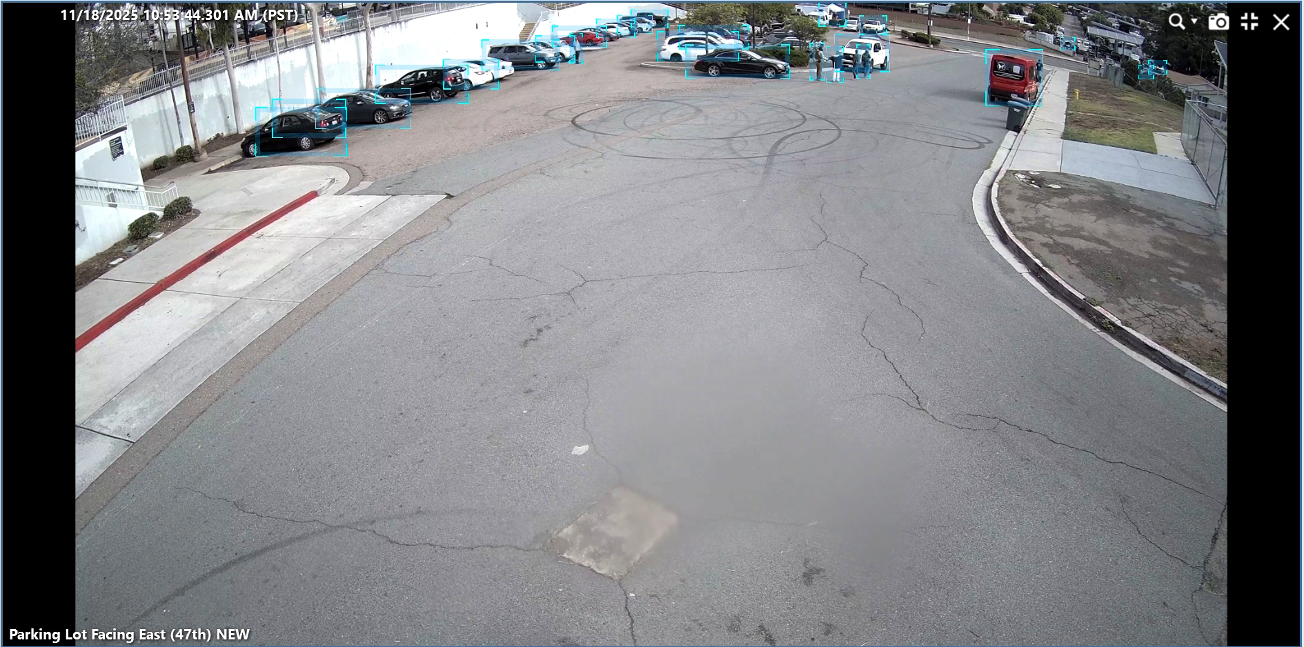 In a large parking lot, an agent in the distance holds the wrist of a woman with blue hair.