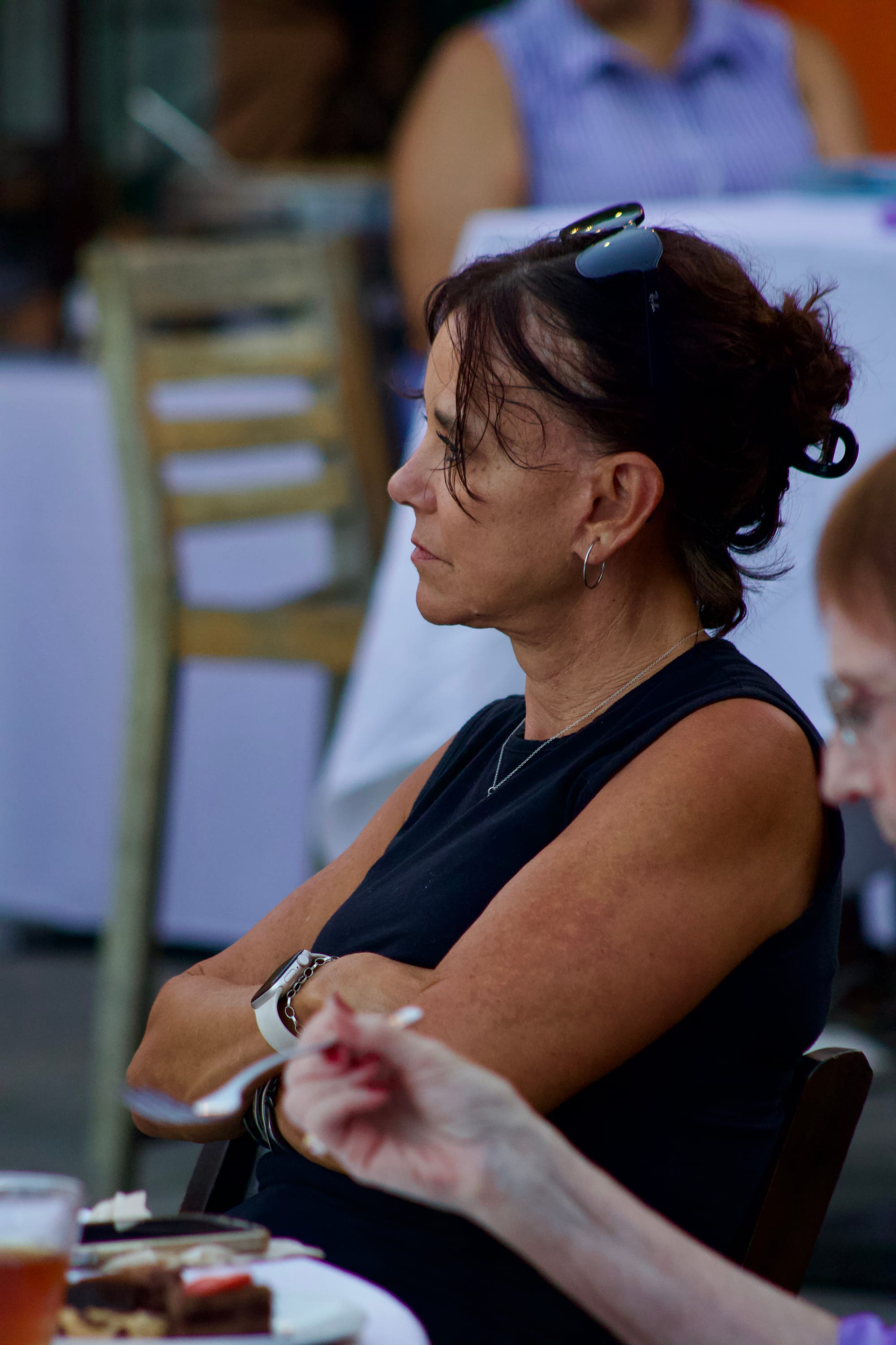 A woman sits with her arms crossed at an outdoor event