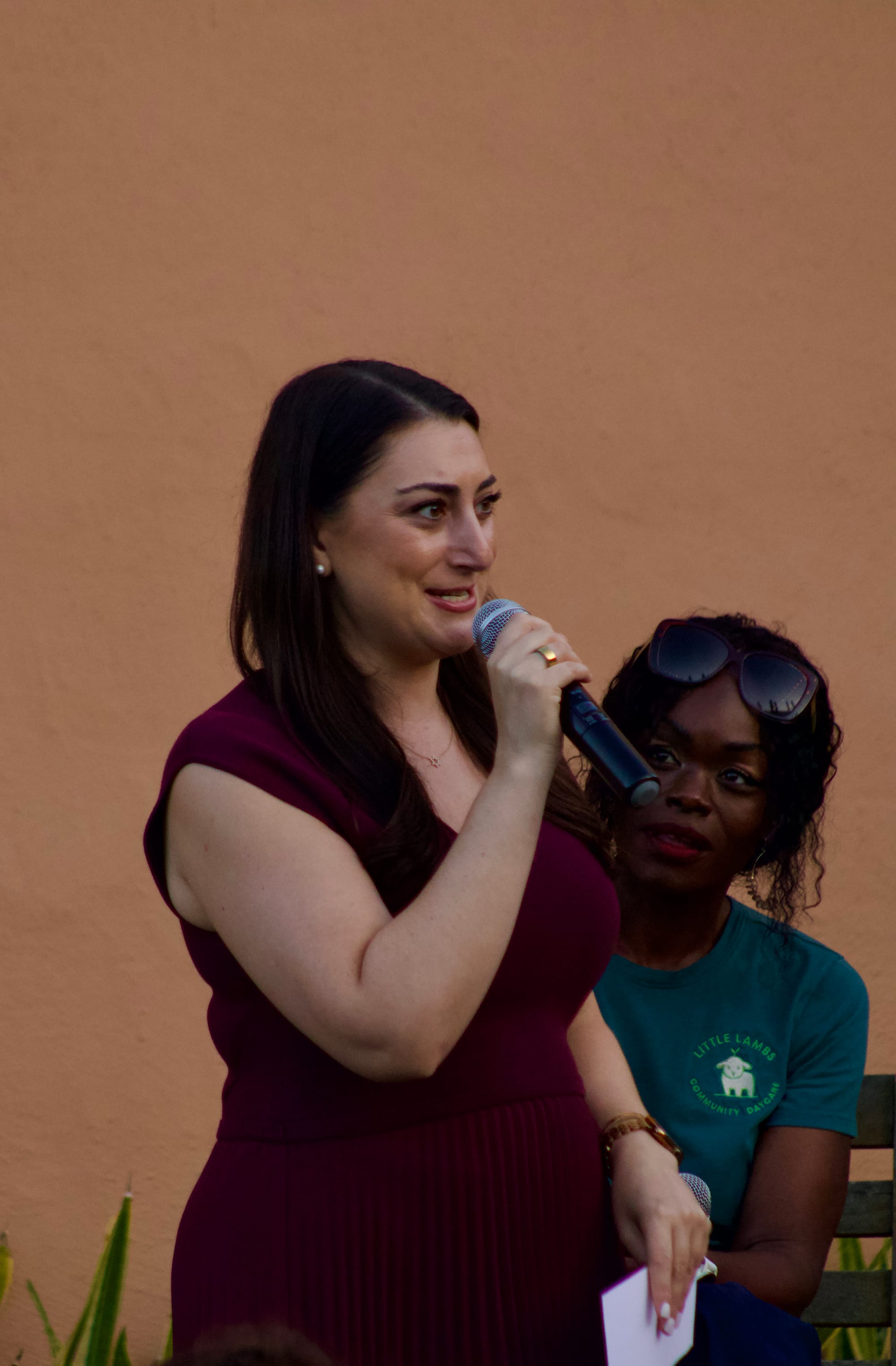 A woman speaks into a microphone in front of another woman