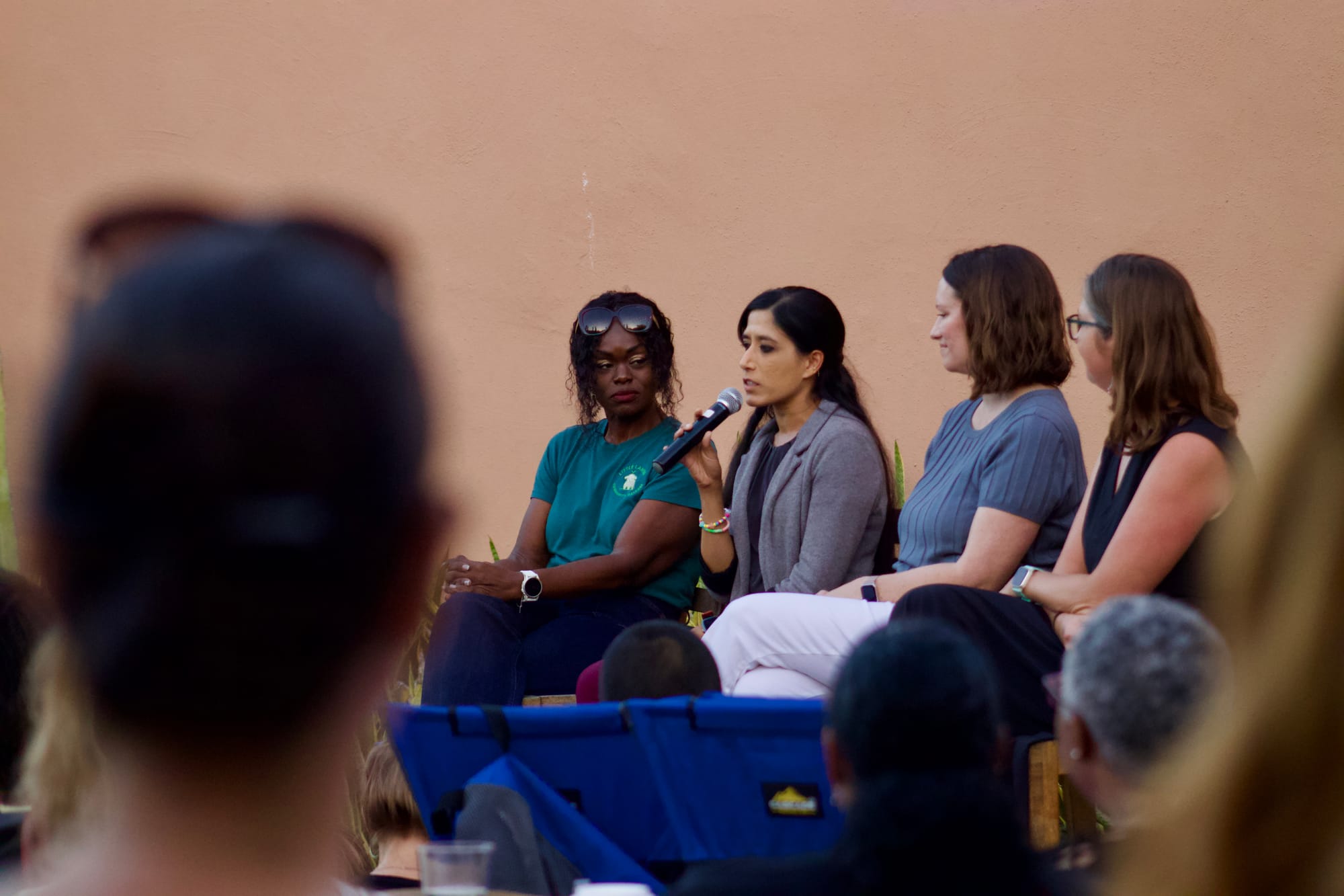 Four women sit on a panel at an outdoor event in front of a crowd.