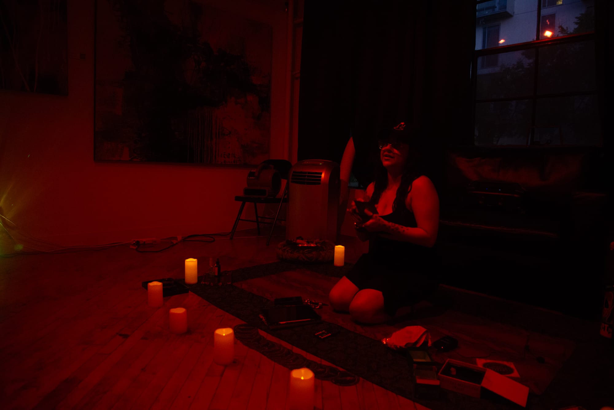 A woman in red lighting kneels on a yoga mat holding tarot cards with candles around her