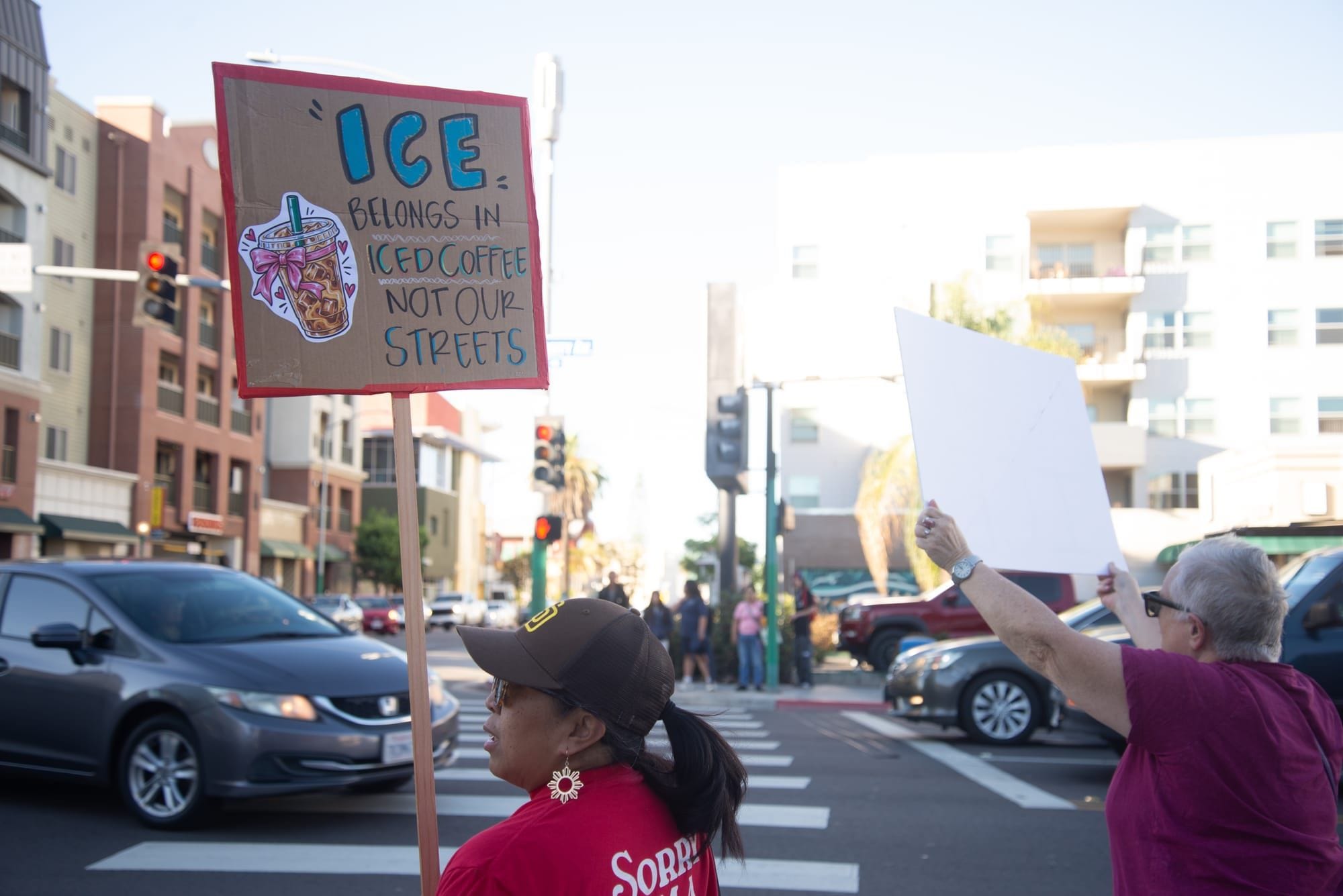 A person holds a sign that reads Ice belongs in iced coffee not our streets during a demonstration on a street corner