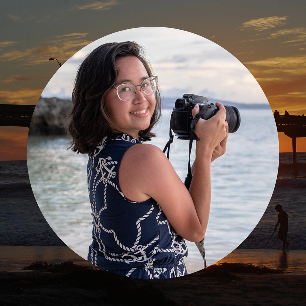 A woman holds a camera in front of an ocean