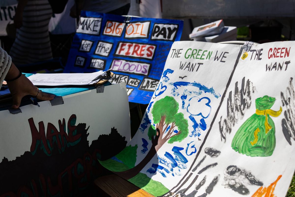 Hand painted signs read "make big oil pay for the fires for the floods," "the green we want/the green they want""