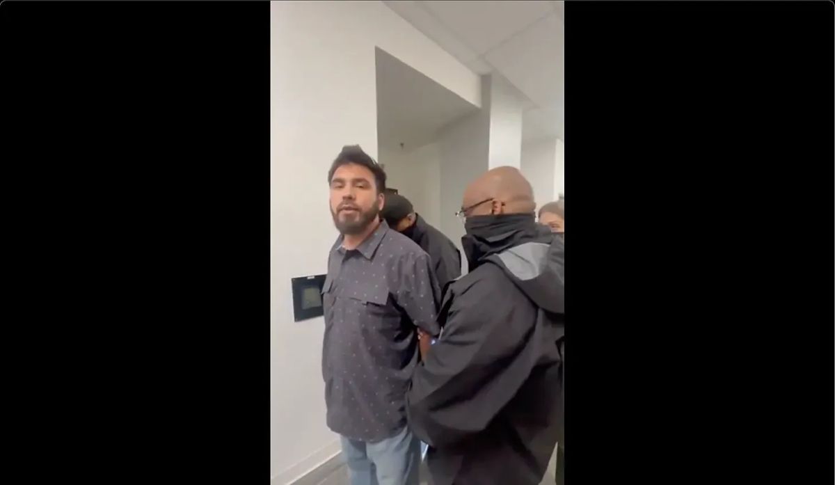 A man in a hallway is arrested by masked people