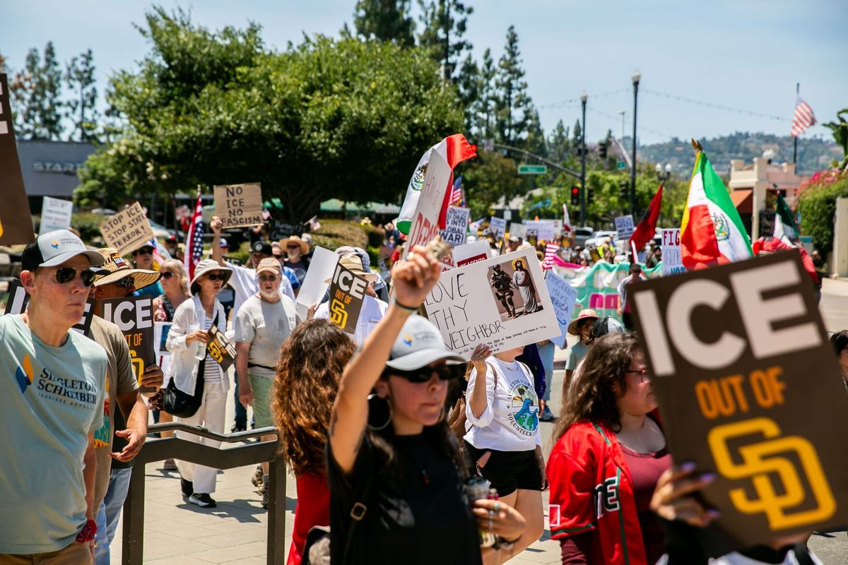 People march in a protest holding signs including one that says “ICE out of SD”