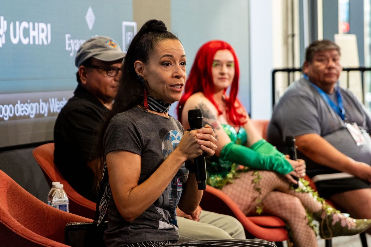 Four people sit on a panel on a stage and one person holds a mic