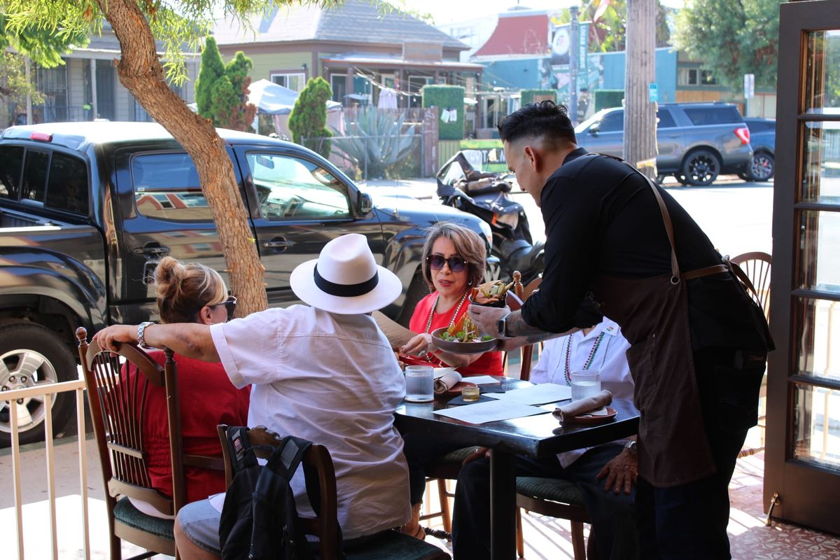 A waiter serves food to a table of four sitting on a restaurant patio