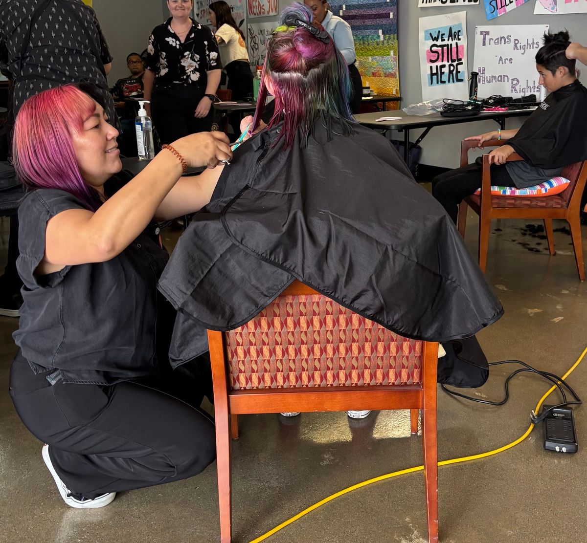 Someone crouches down while cutting someone's hair at an event 