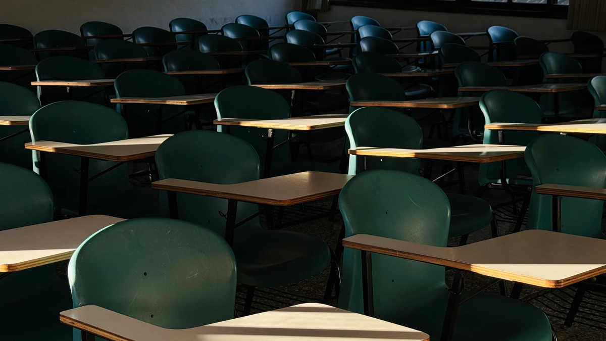 A dark classroom full of desk-chair combos with light shining in from the bottom left corner