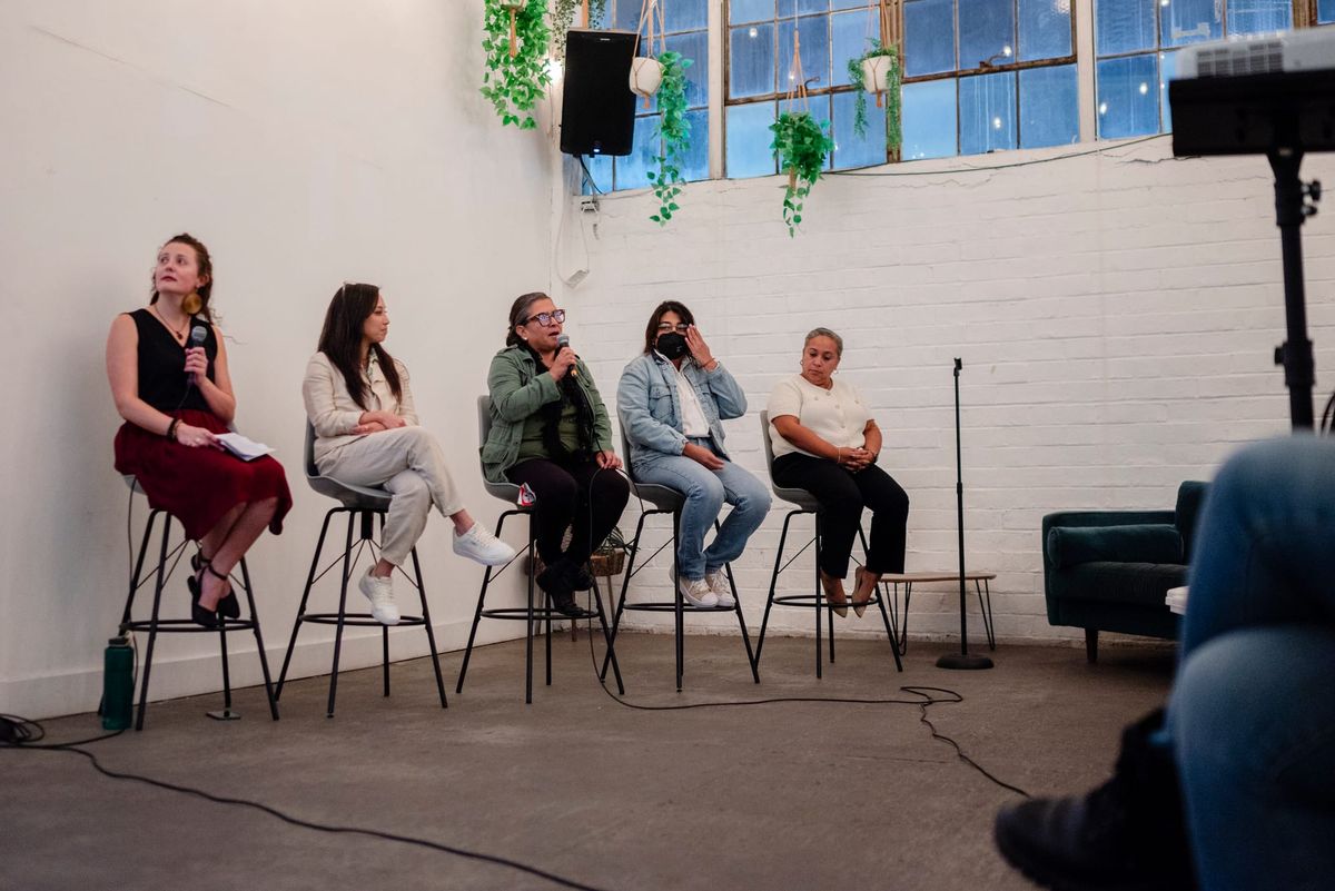 Four panelists and a moderator sit on chairs, while one panelist seated in the middle in green speaks to the audience.