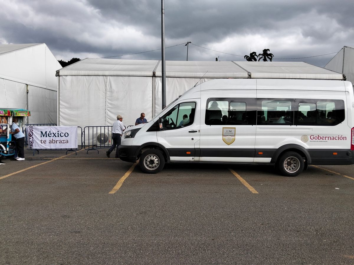 A white van with Gobernación written on the side is parked in front of a white tent with silhouettes of people leaving the van seen through the window