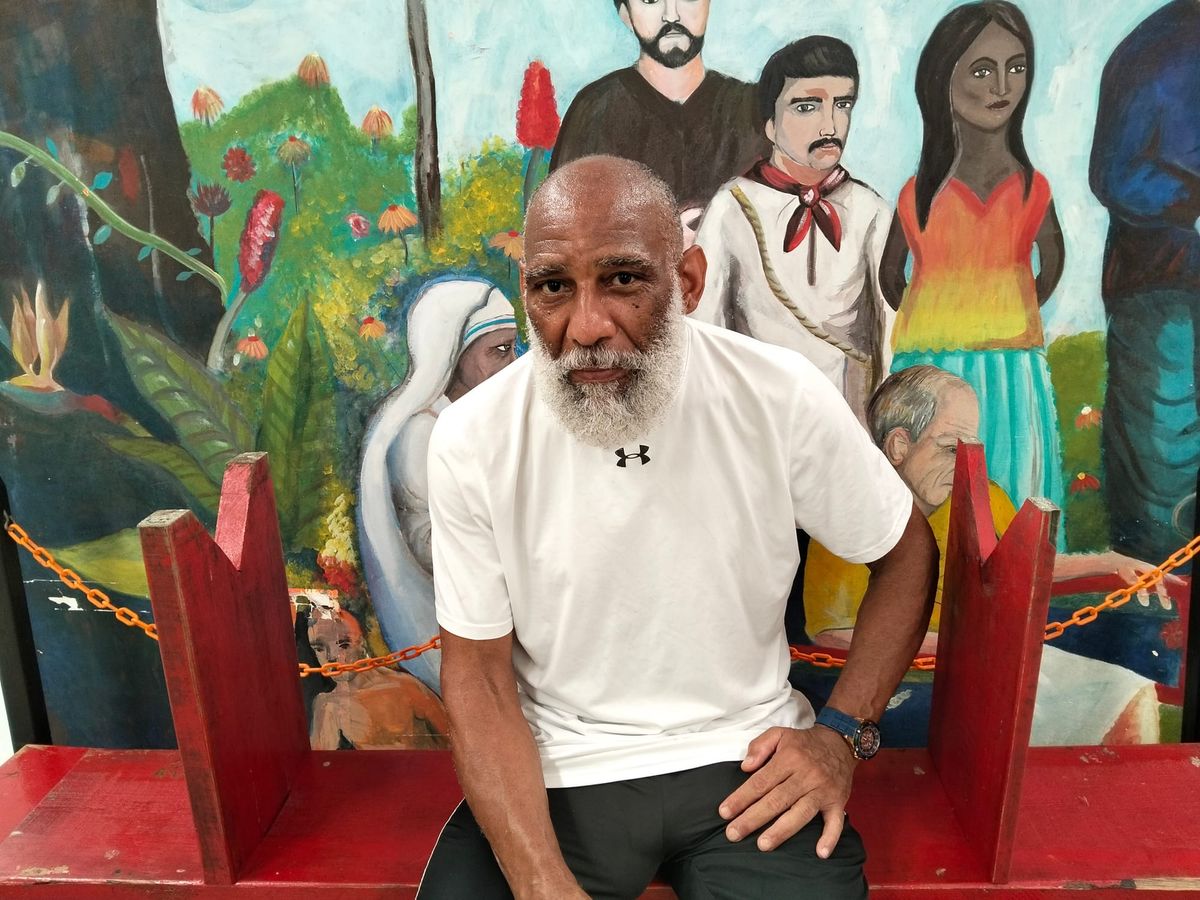 A man in a white shirt sits in front of a colorful mural