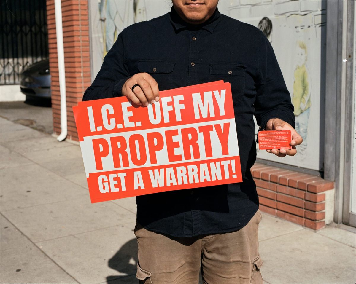 A man holds a sign that says I.C.E. off my property get a warrant! and a red card
