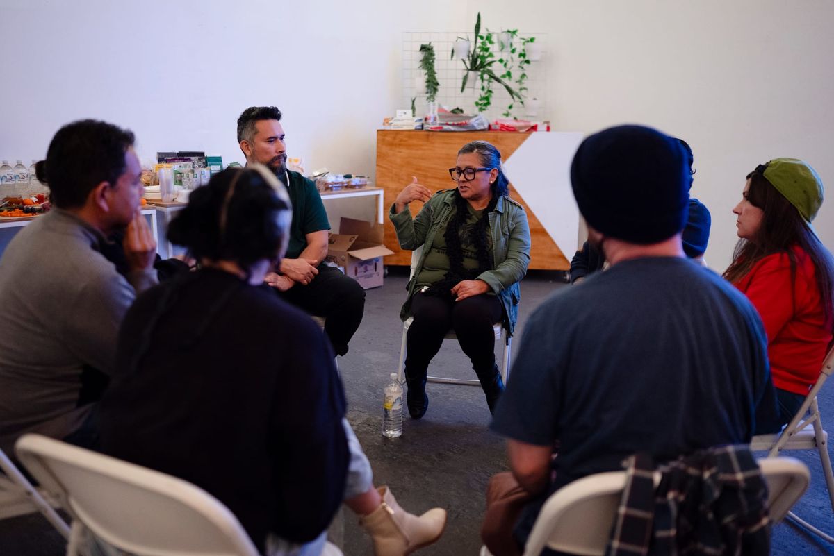 A woman speaks to a group of people sitting in chairs facing one another. 