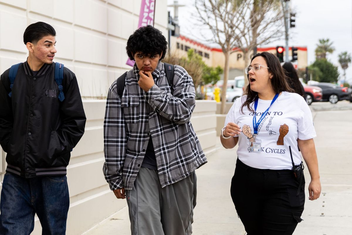 A women and two teens walk down the street talking.